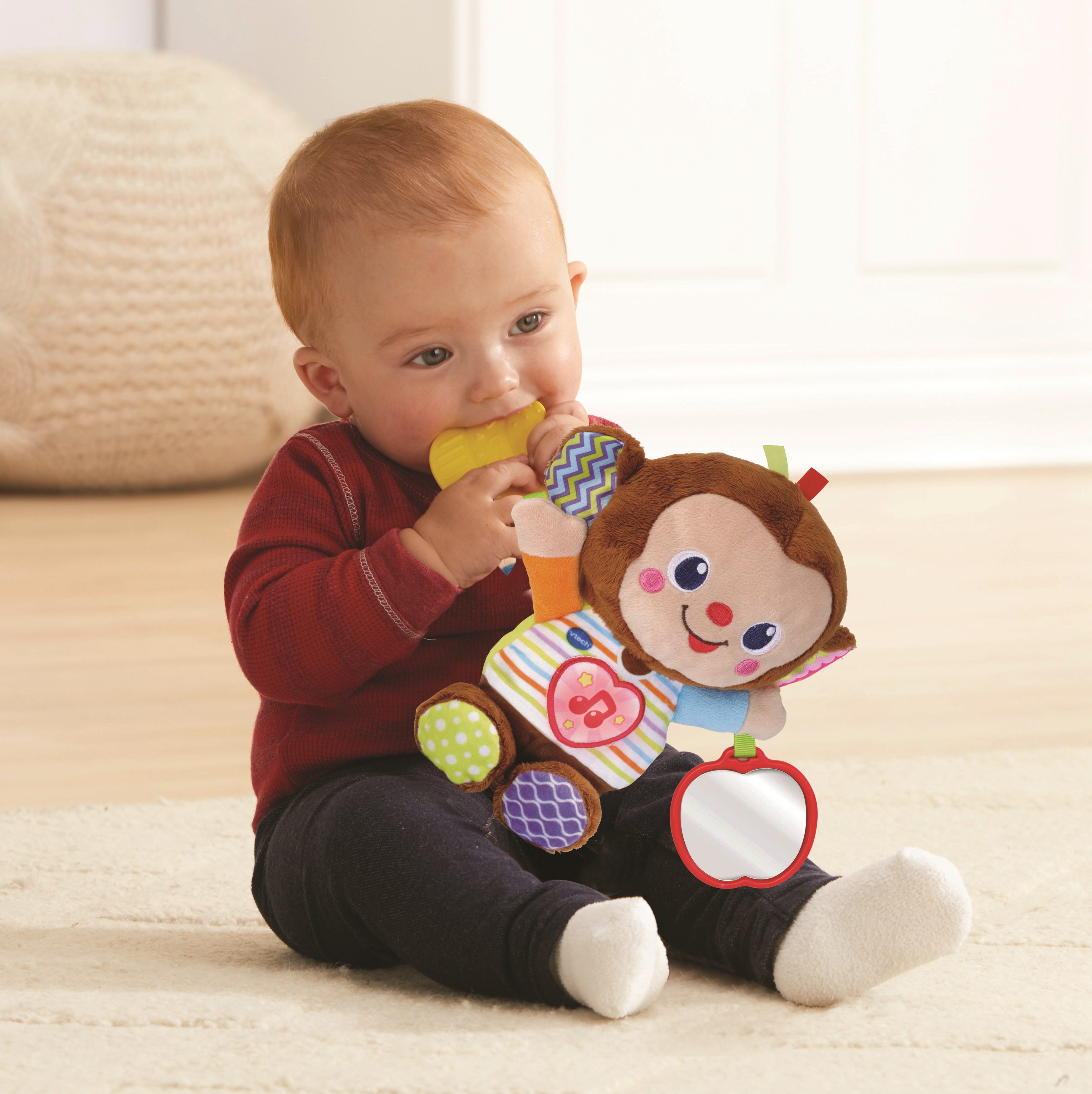 Ein Baby kaut auf einem gelben Beißring, während es einen bunten Stoffaffen hält.