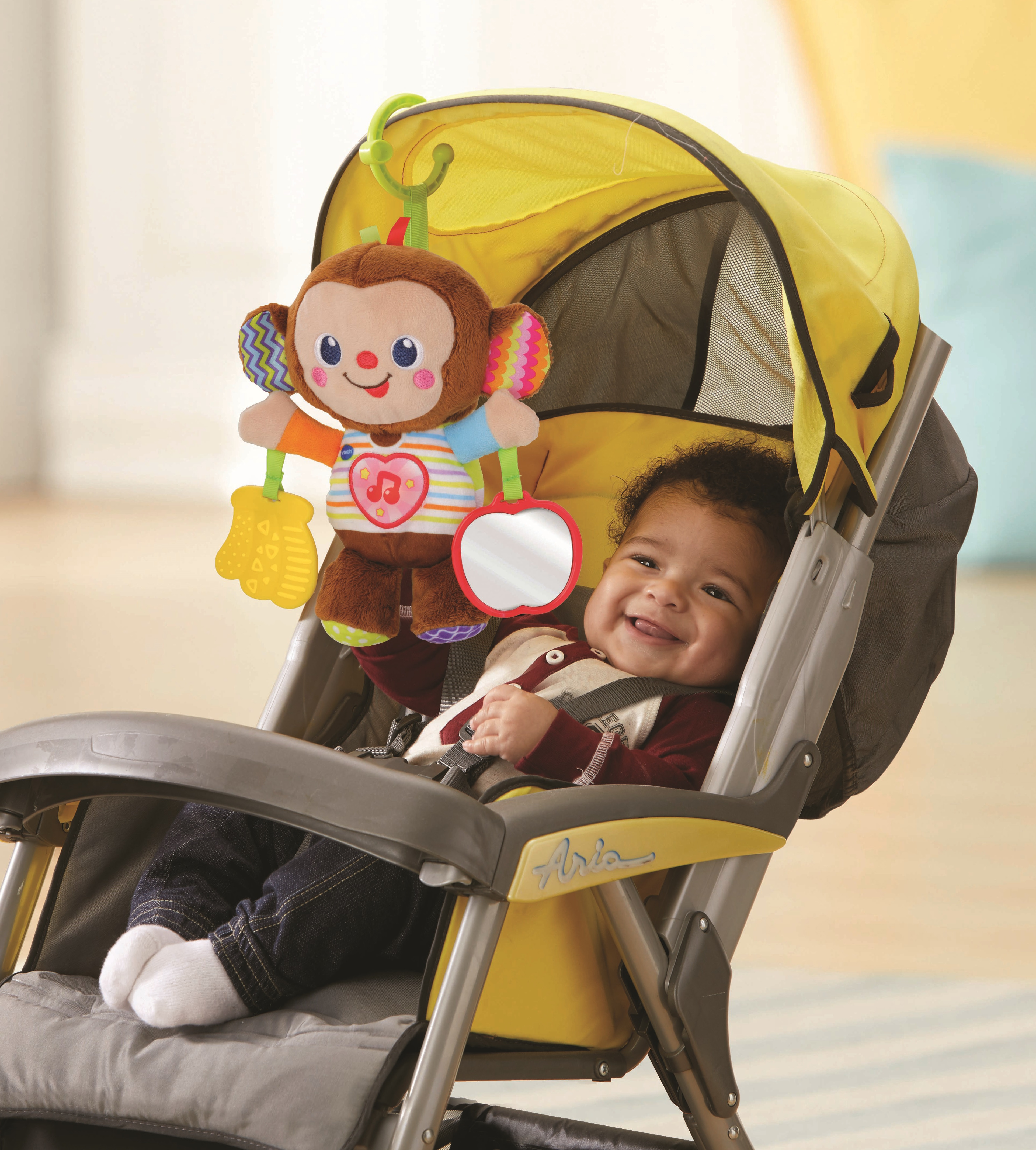 Ein lächelndes Baby sitzt im Kinderwagen mit einem Plüschaffen-Spielzeug darüber.