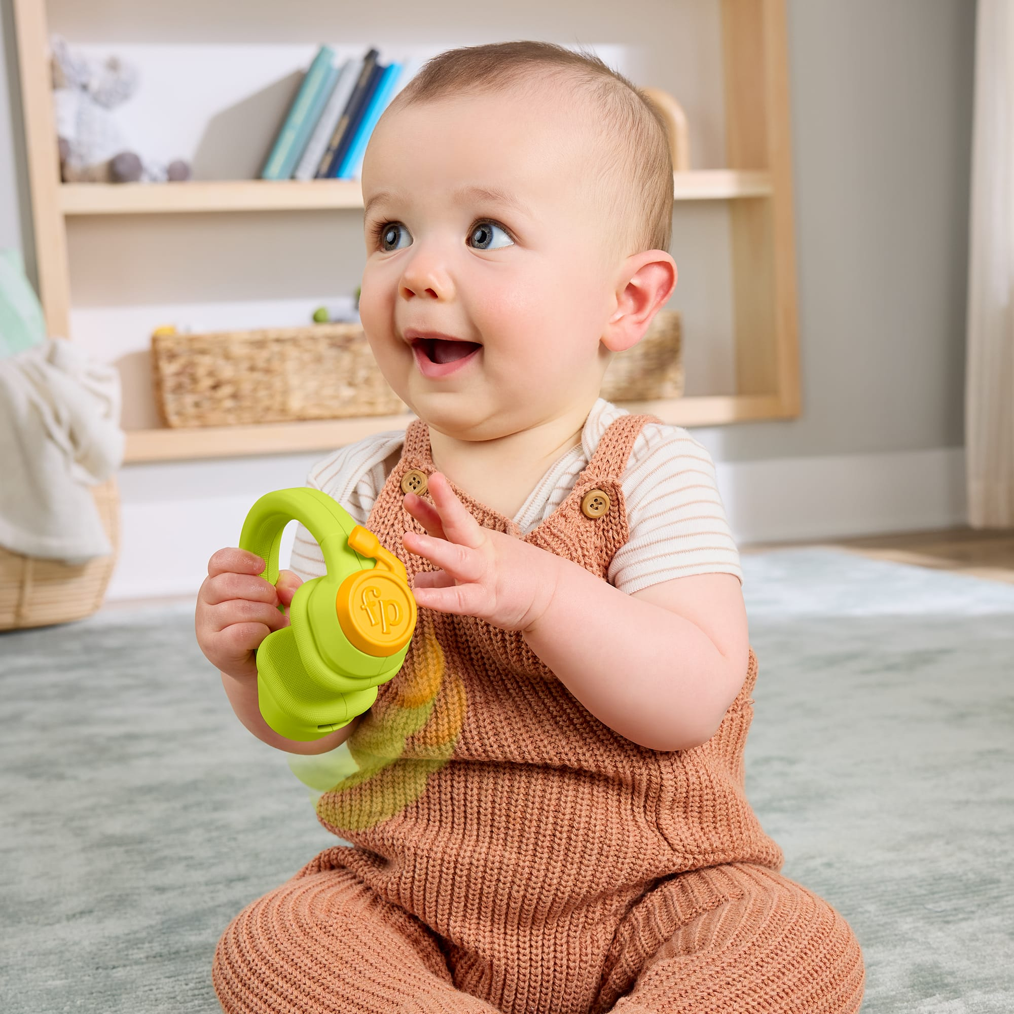 Ein Baby sitzt auf einem Teppich und hält ein grünes Spielzeughandy.