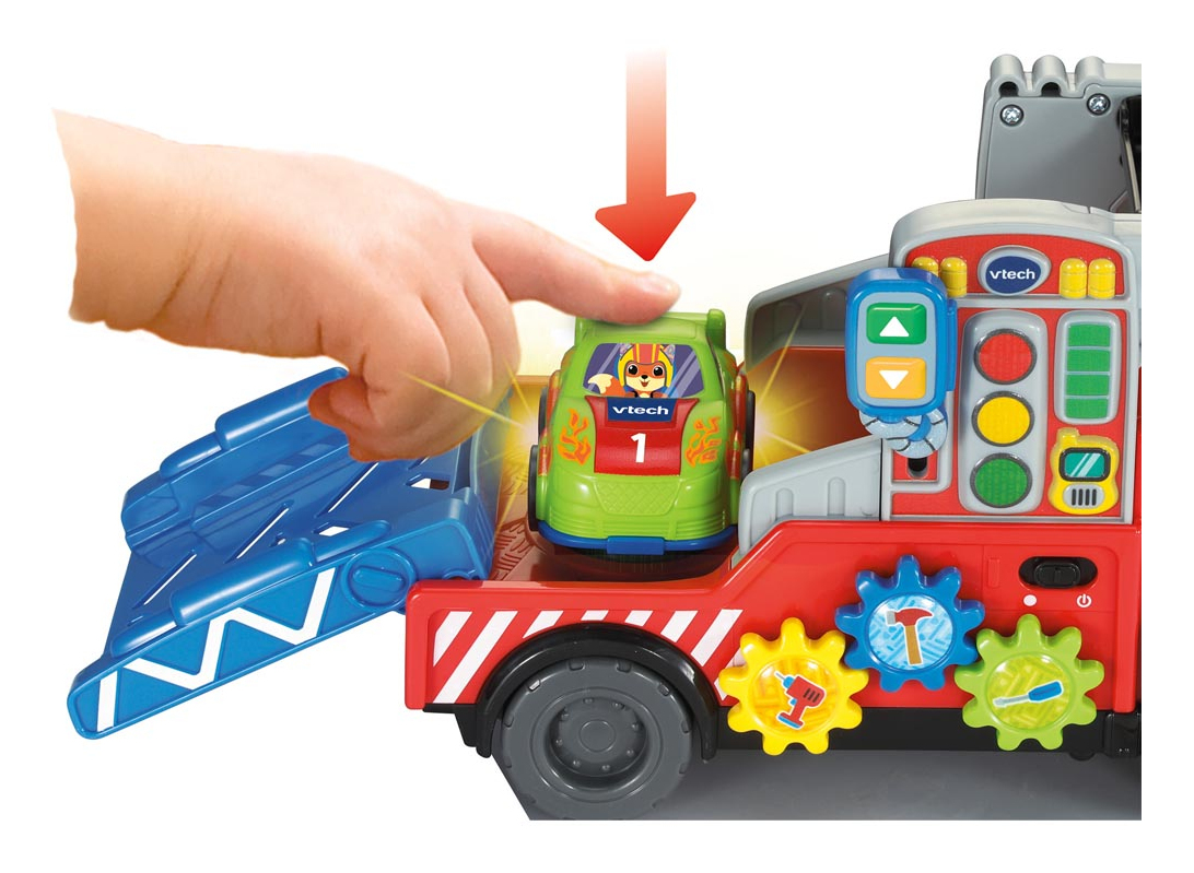 Ein Kinderfinger drückt auf ein grünes Spielzeugauto auf einem roten Abschleppwagen mit Zahnrädern.