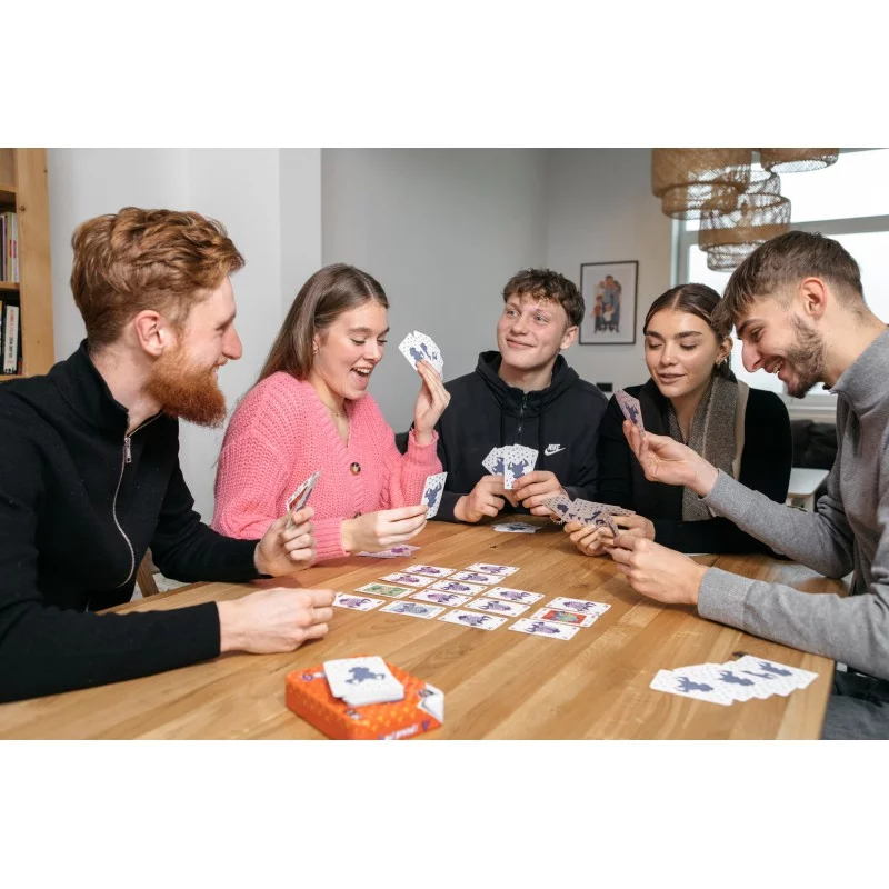 Cinq jeunes adultes assis à une table en bois jouent à un jeu de cartes avec des cartes violettes et blanches.