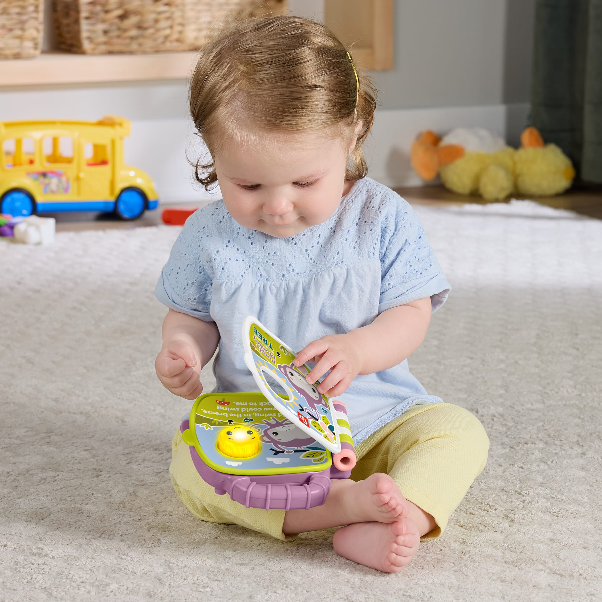 Ein Baby spielt mit einem bunten Spielzeugbuch auf einem Teppich. Ein gelber Schulbus ist im Hintergrund.