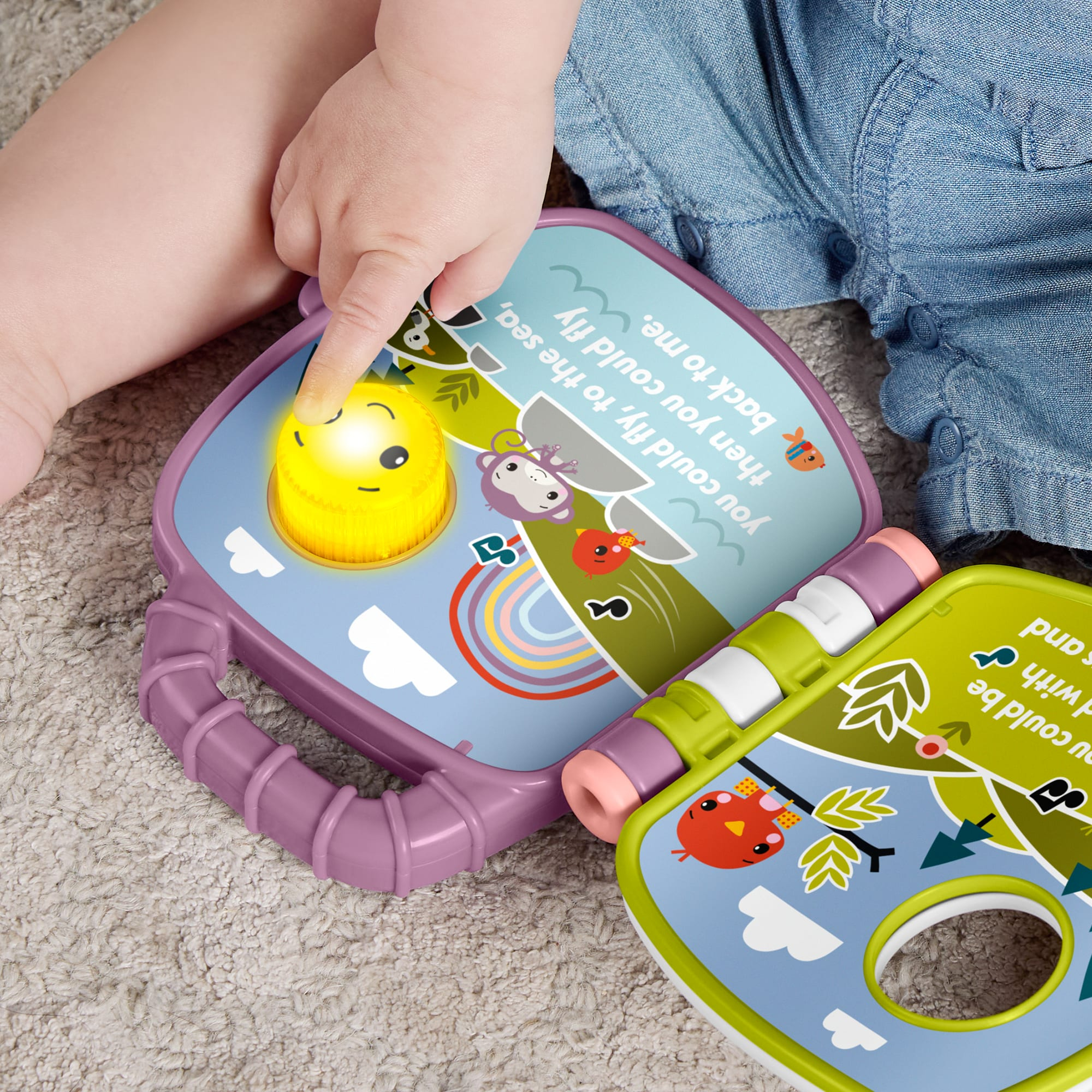 Ein Babyfinger drückt einen leuchtend gelben Knopf auf einem lila Spielzeugbuch mit bunten Illustrationen.