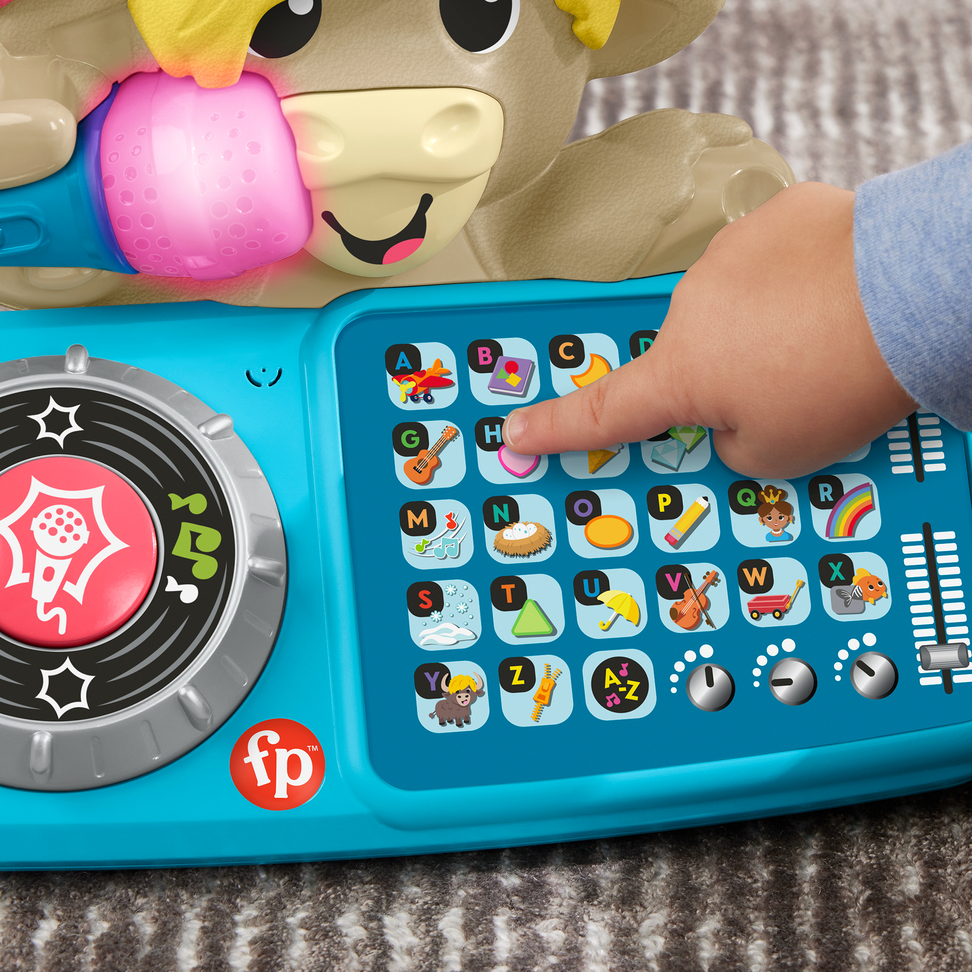 Die Hand eines Kindes interagiert mit einem blauen Fisher-Price-Spielzeug und drückt einen Knopf auf einem Raster aus Buchstaben und Bildern.