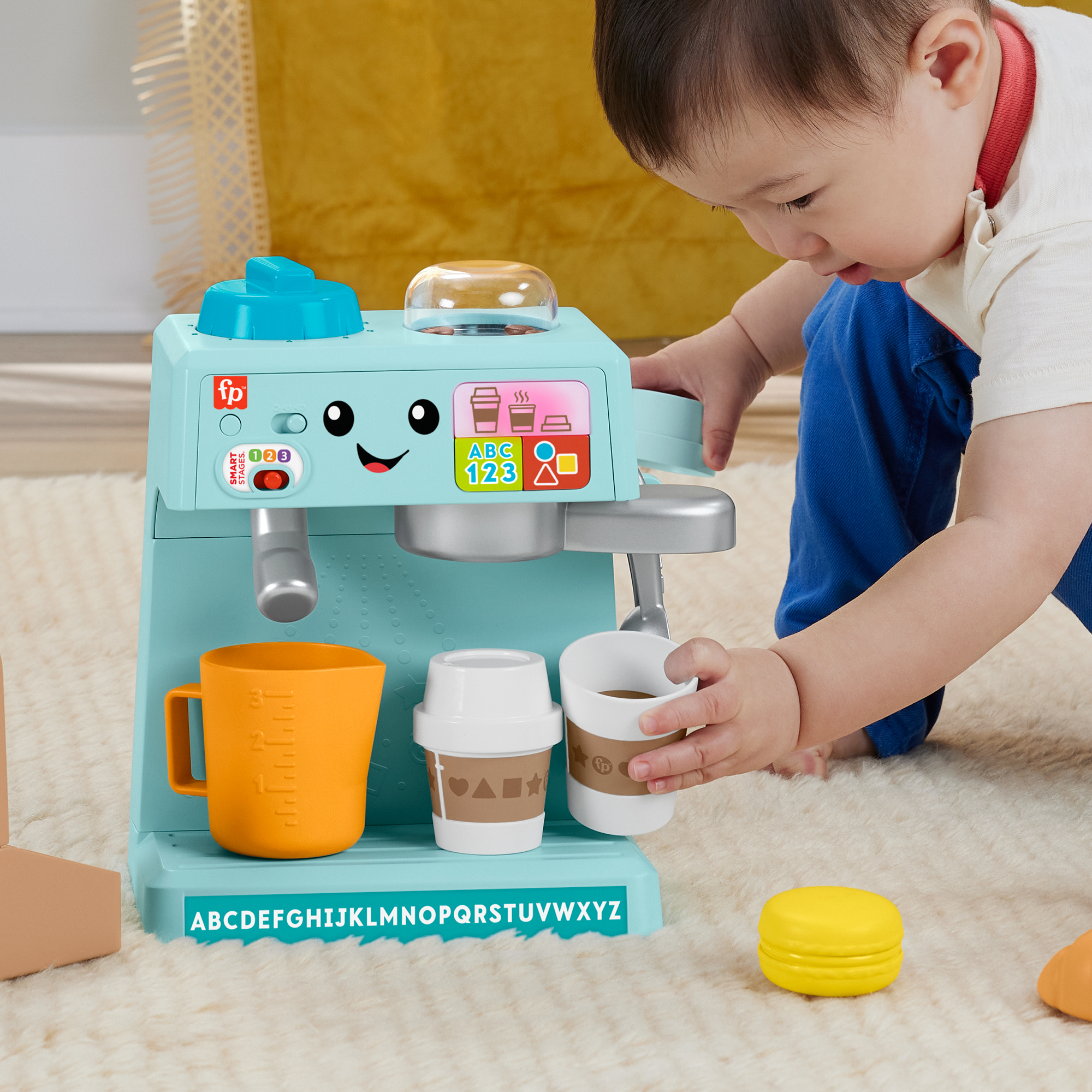 Ein Kleinkind spielt mit einer hellblauen Spielzeug-Kaffeemaschine, die Tassen hält.