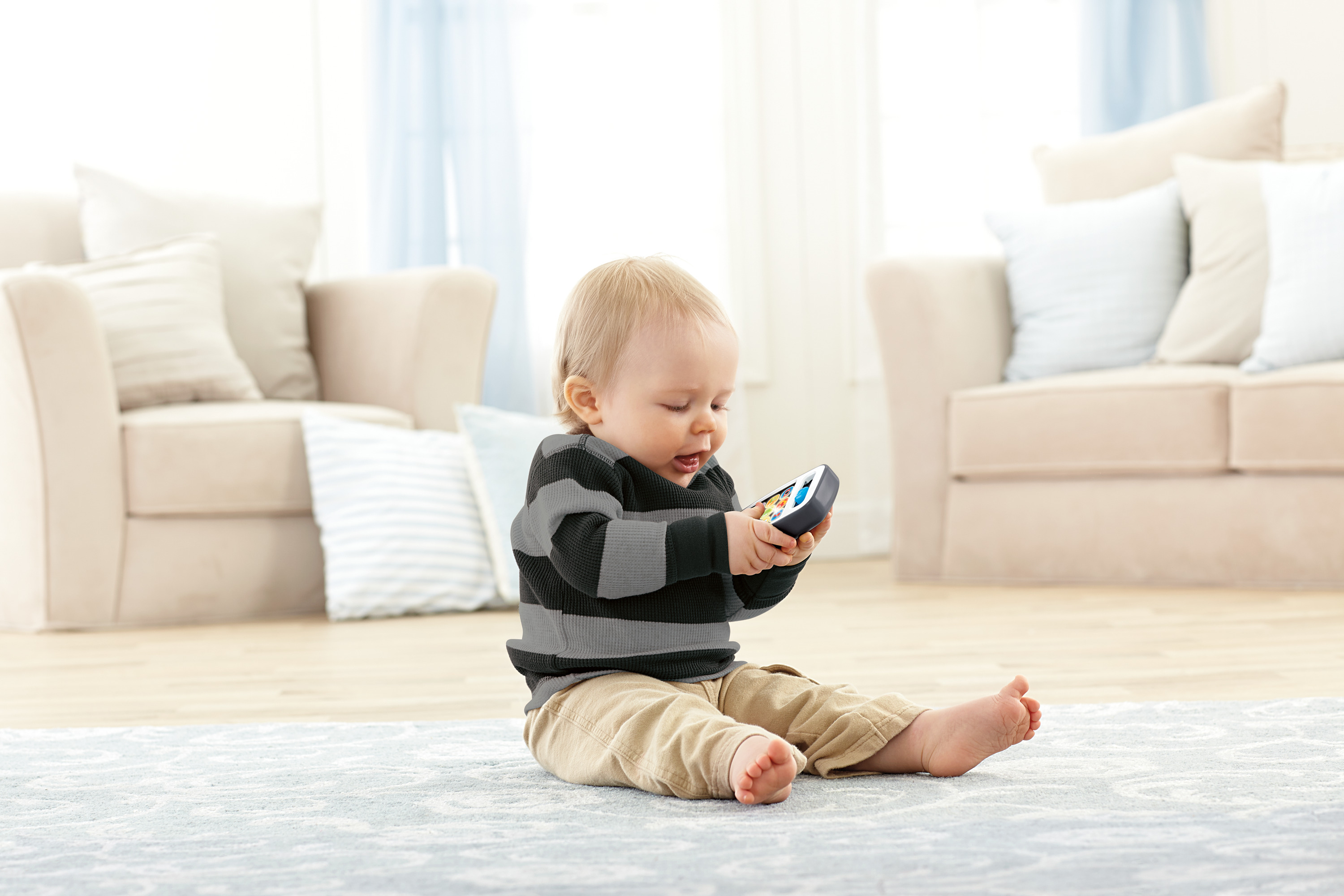 Ein Baby in einem gestreiftem Oberteil und beige Hose spielt mit einem Spielzeug.
