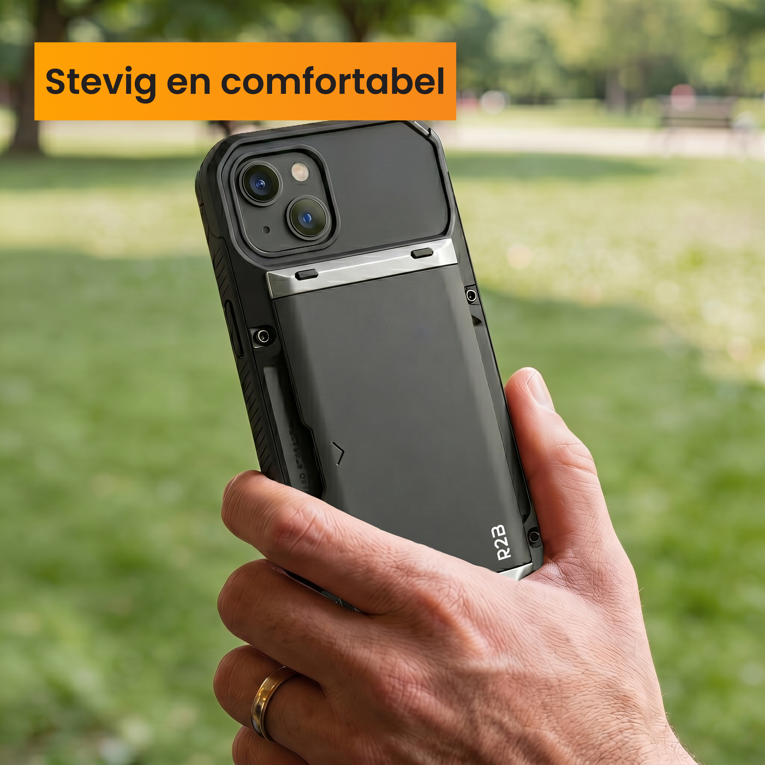 Hand holding dark phone with black case outdoors, green blurred background.