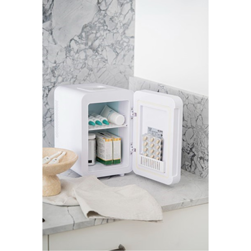 Un mini-frigo bianco con lo sportello aperto, che rivela prodotti per la cura della pelle e farmaci, su un piano di lavoro in marmo.