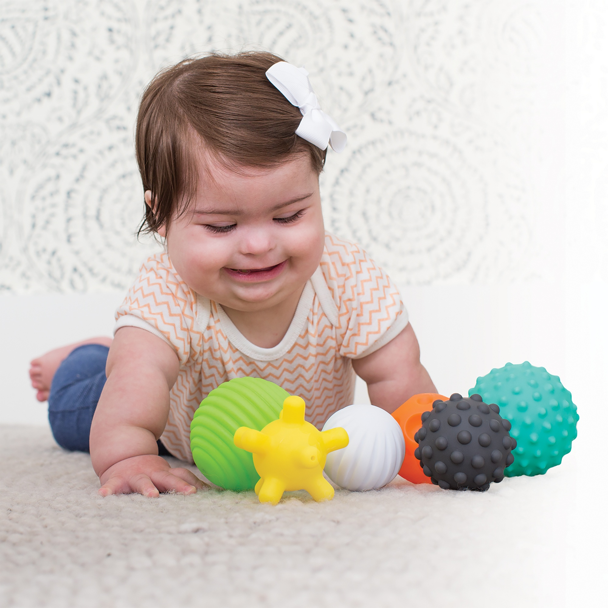 Ein Baby liegt auf dem Bauch und spielt mit bunten Bällen auf einem Teppich.