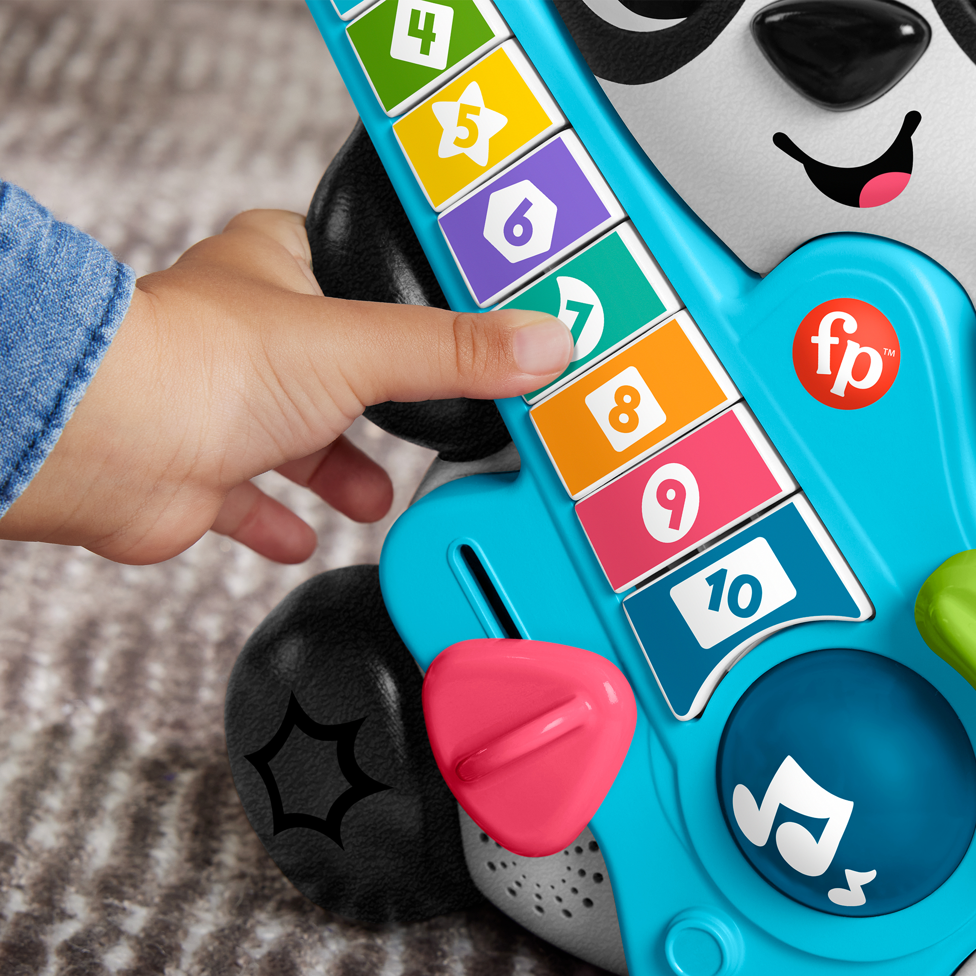 Ein Kinderfinger drückt auf eine blaue Spielzeuggitarre mit bunten Tasten.