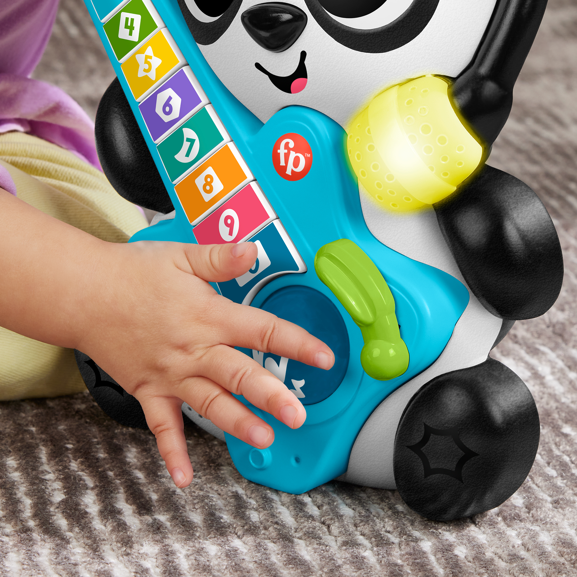 Kinderhand spielt blaue Spielzeuggitarre mit bunten Nummerntasten, Panda-Gesicht und gelbem Licht.