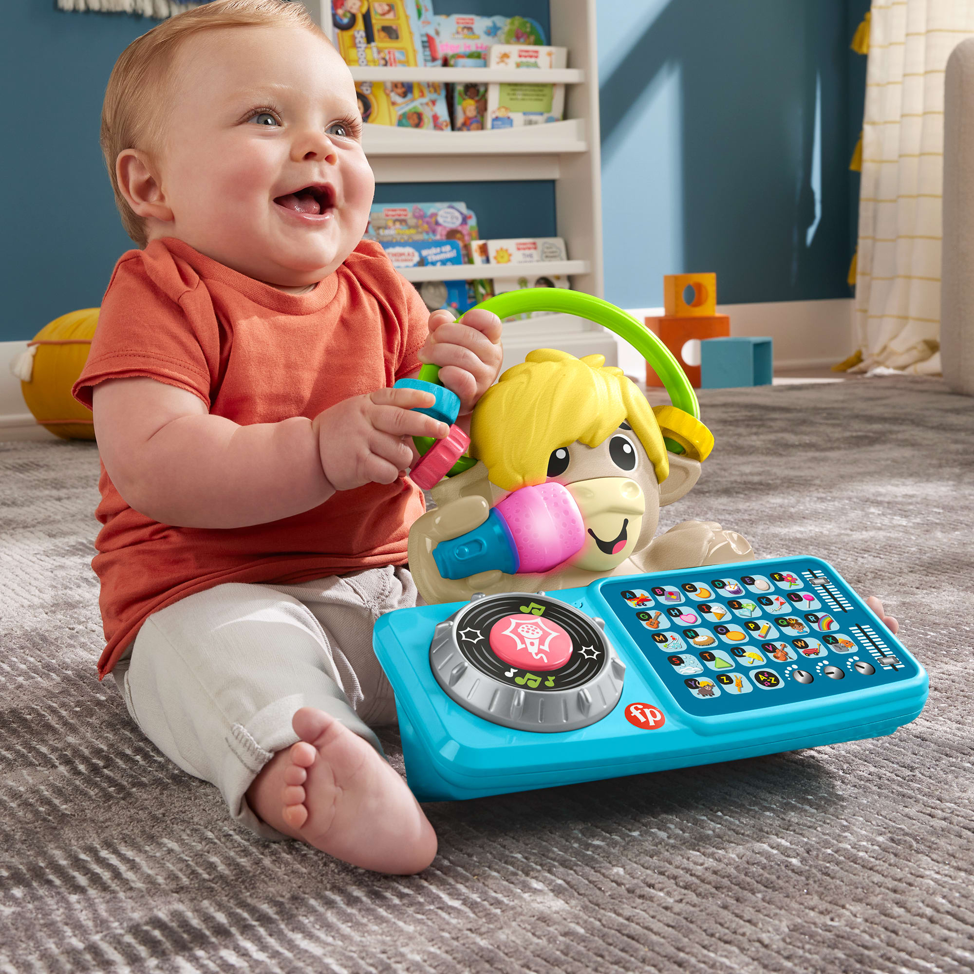 Ein lächelndes Baby in einem orangefarbenen Hemd spielt mit einem blauen Musikspielzeug mit Eselsgesicht.