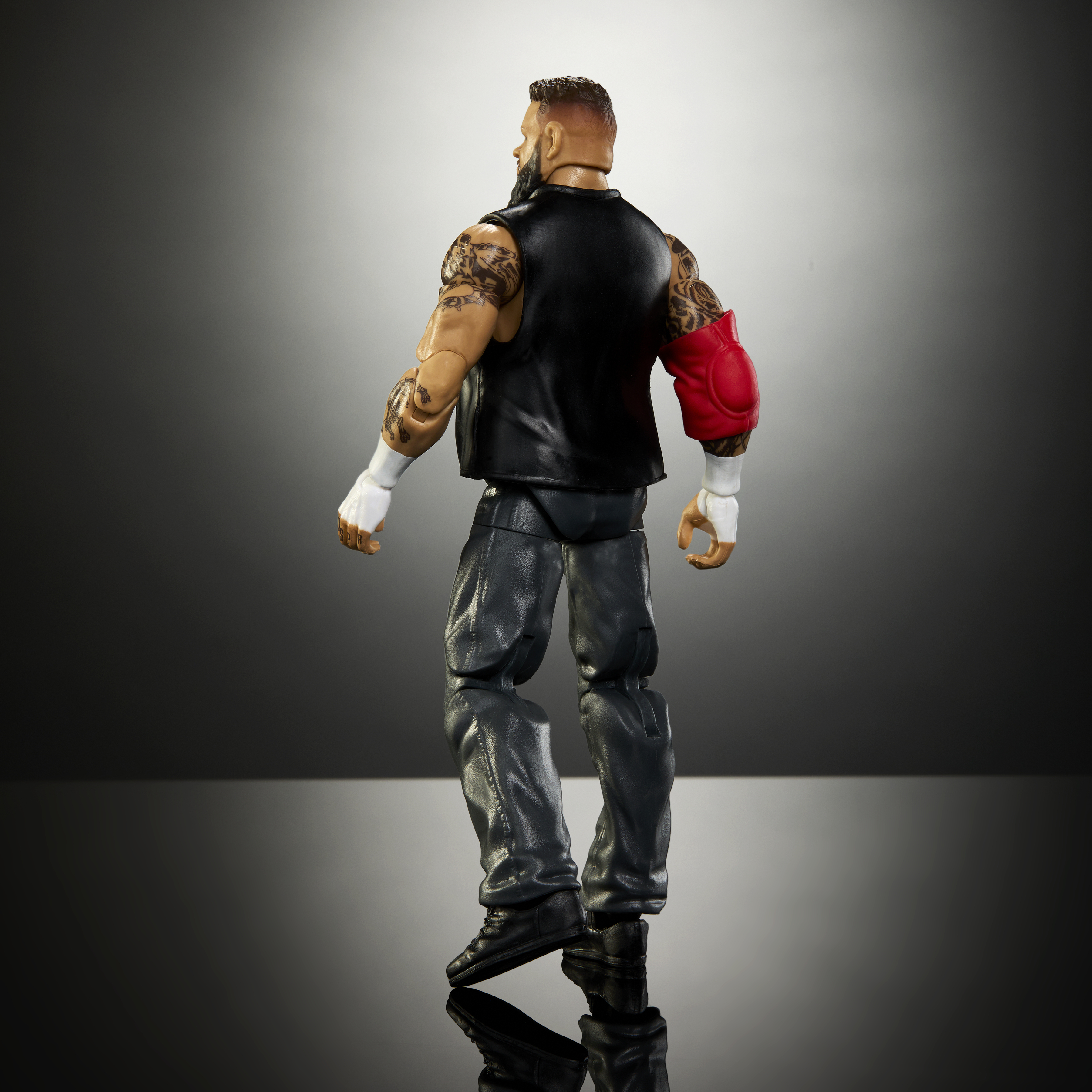 Eine Wrestling-Figur mit Weste, Hose und rotem Armschutz steht im Profil.