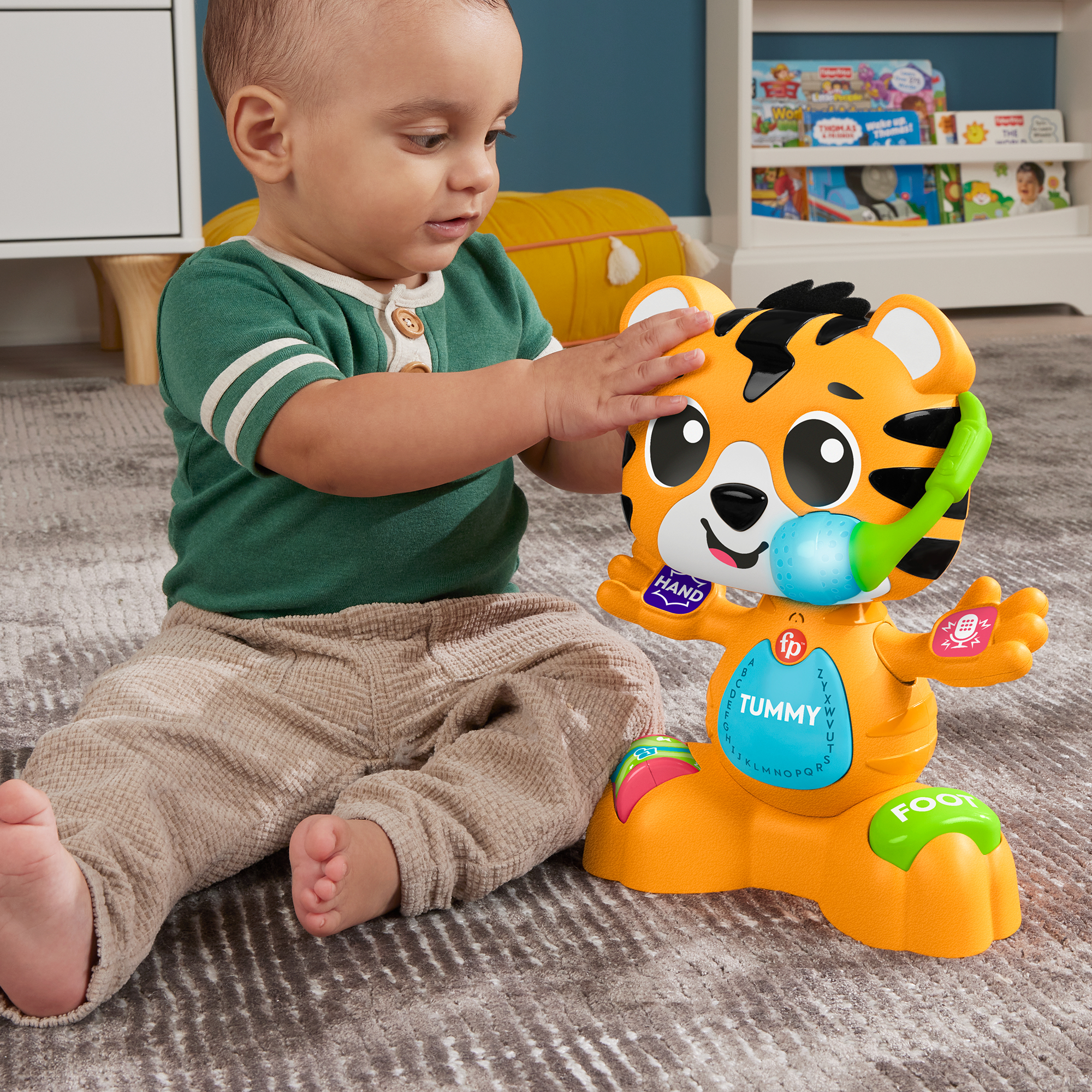 Ein Baby in Grün und Beige spielt mit einem orange-schwarzen Tigertier mit leuchtenden Funktionen auf einem grauen Teppich.