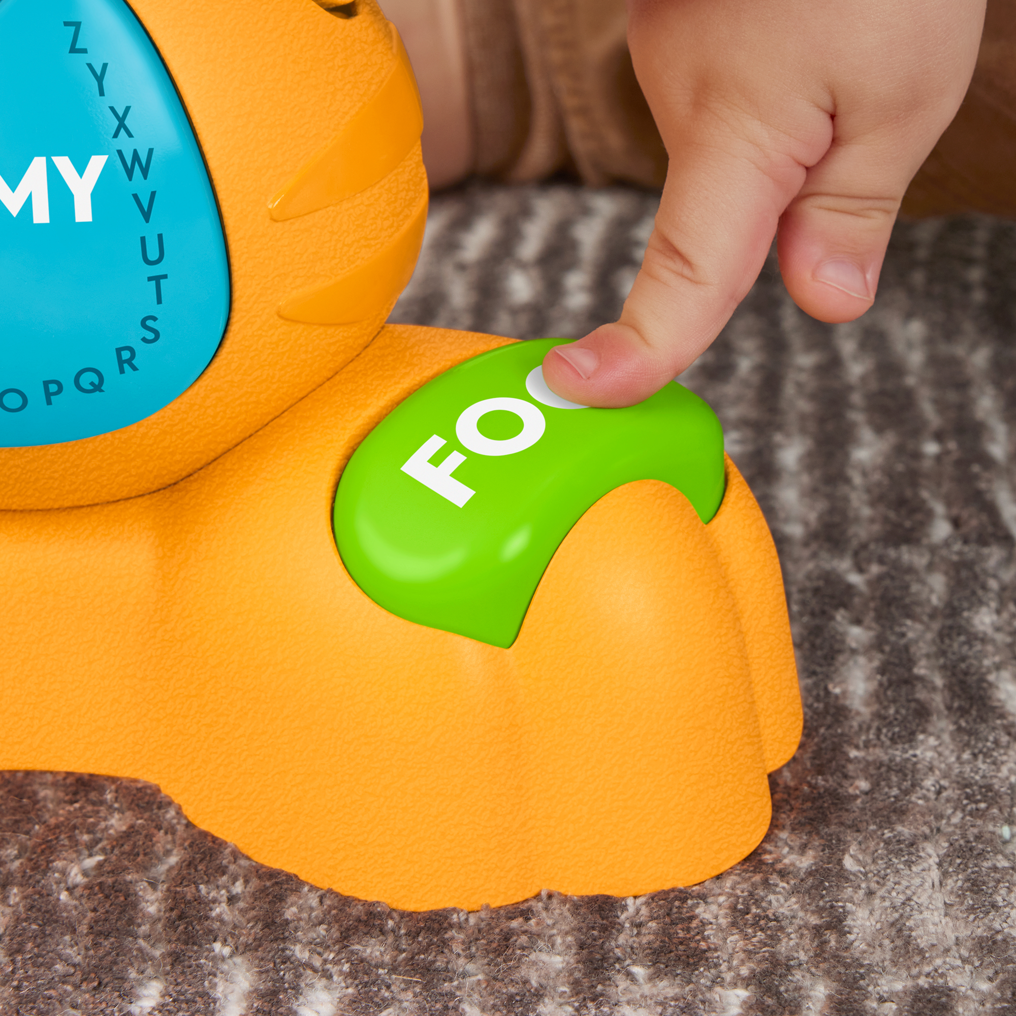Ein Kind drückt auf eine grüne Taste mit der Aufschrift „Foo“ auf einem orangefarbenen Spielzeug.