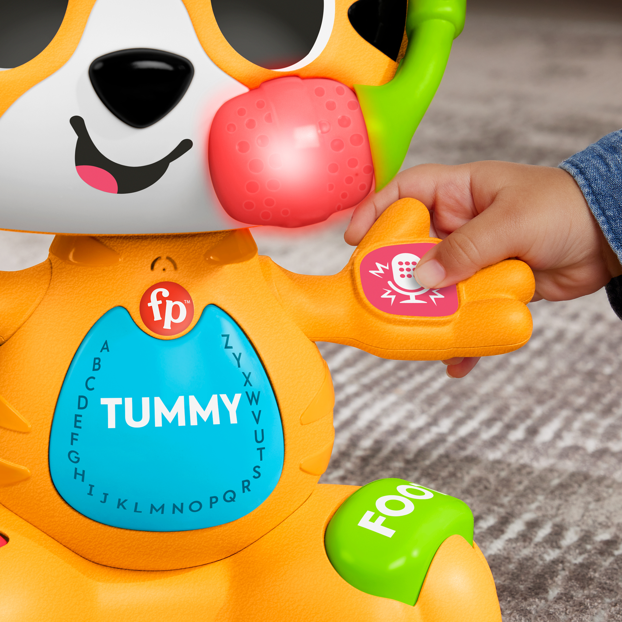 Kinderhand drückt Knopf an Spielzeugkatze mit blinkender roter Wange und ABCs am Bauch.