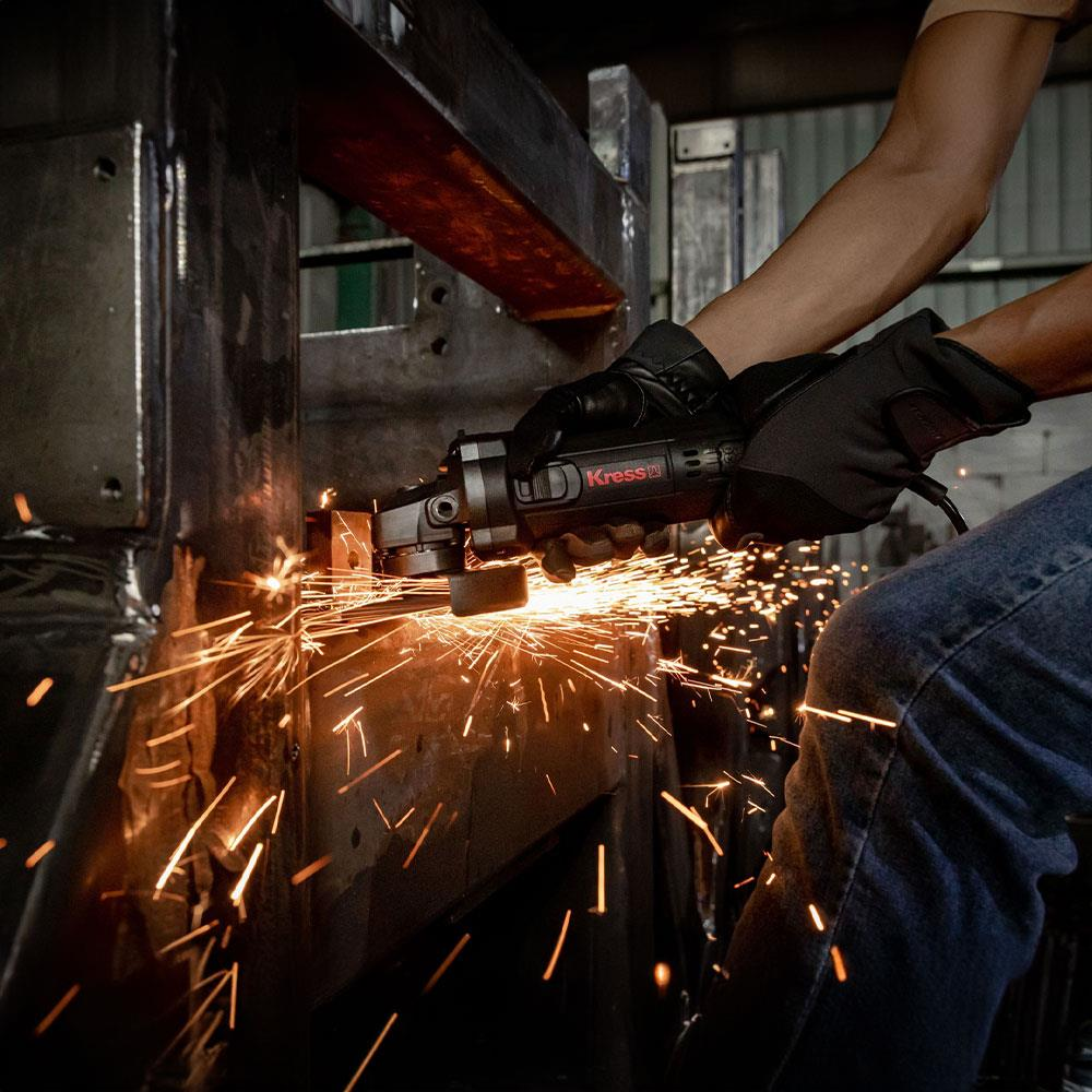 Mavi kot pantolonlu ve siyah eldivenli bir kişi, açılı taşlama makinesiyle metal öğütüyor ve parlak turuncu kıvılcımlar çıkarıyor.