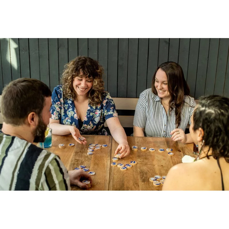 Quatre personnes jouent à un jeu de société sur une table en bois. Elles rient et déplacent des pièces.