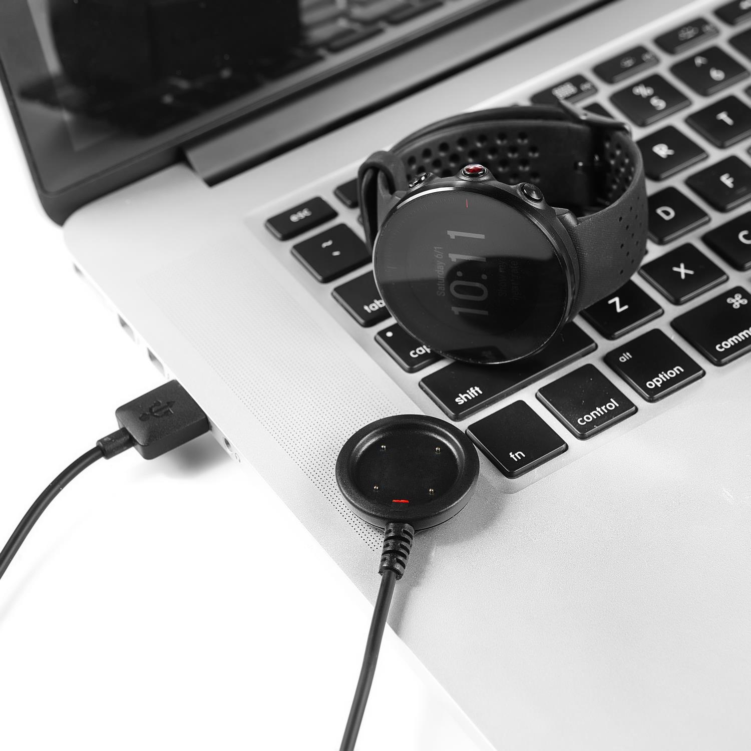 Eine Smartwatch und ihr Ladegerät liegen auf einer Laptop-Tastatur. Ein USB-Kabel verbindet das Ladegerät mit dem Laptop.