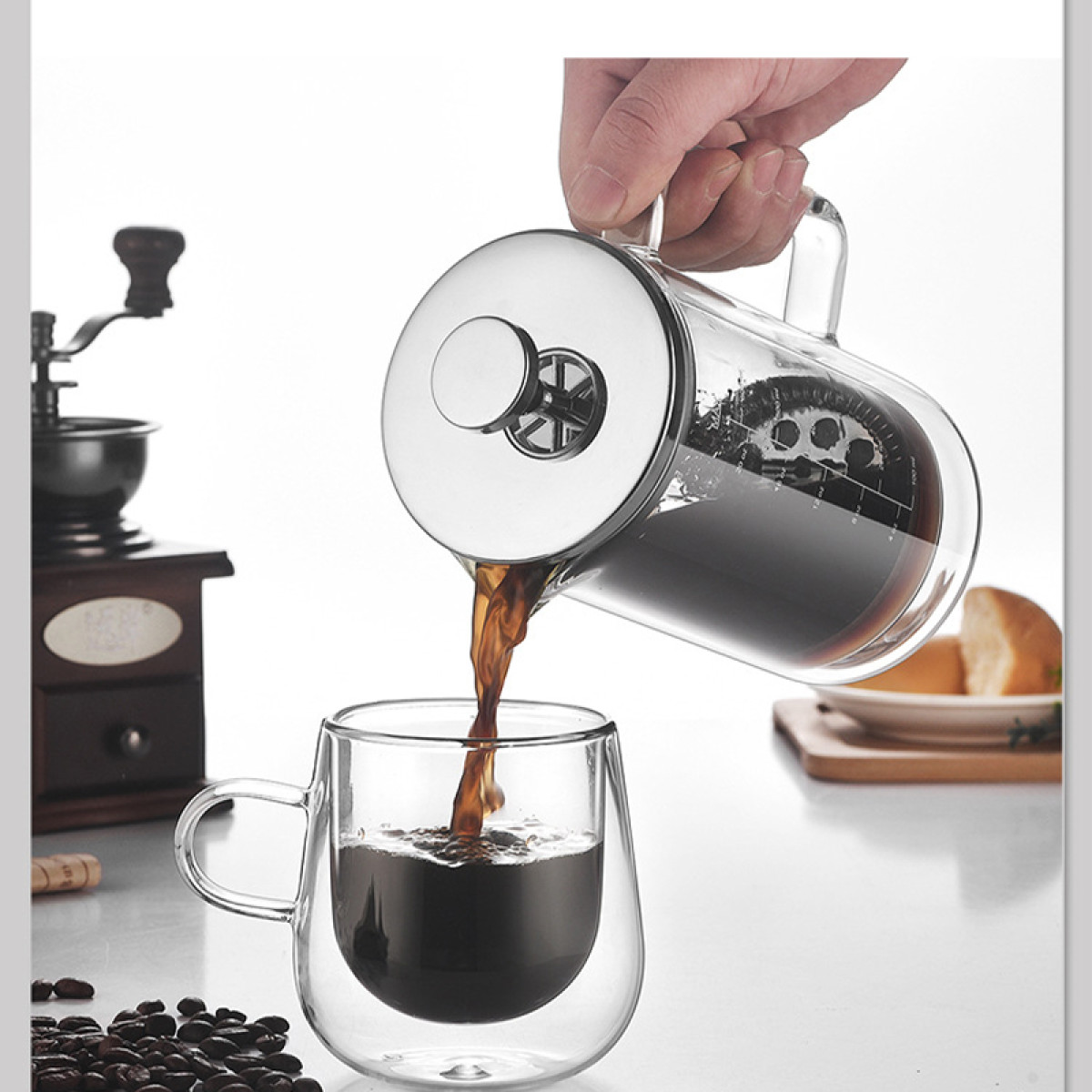 Kaffee wird aus einer Glas-French-Press in eine Glas-Doppelwandtasse gegossen.
