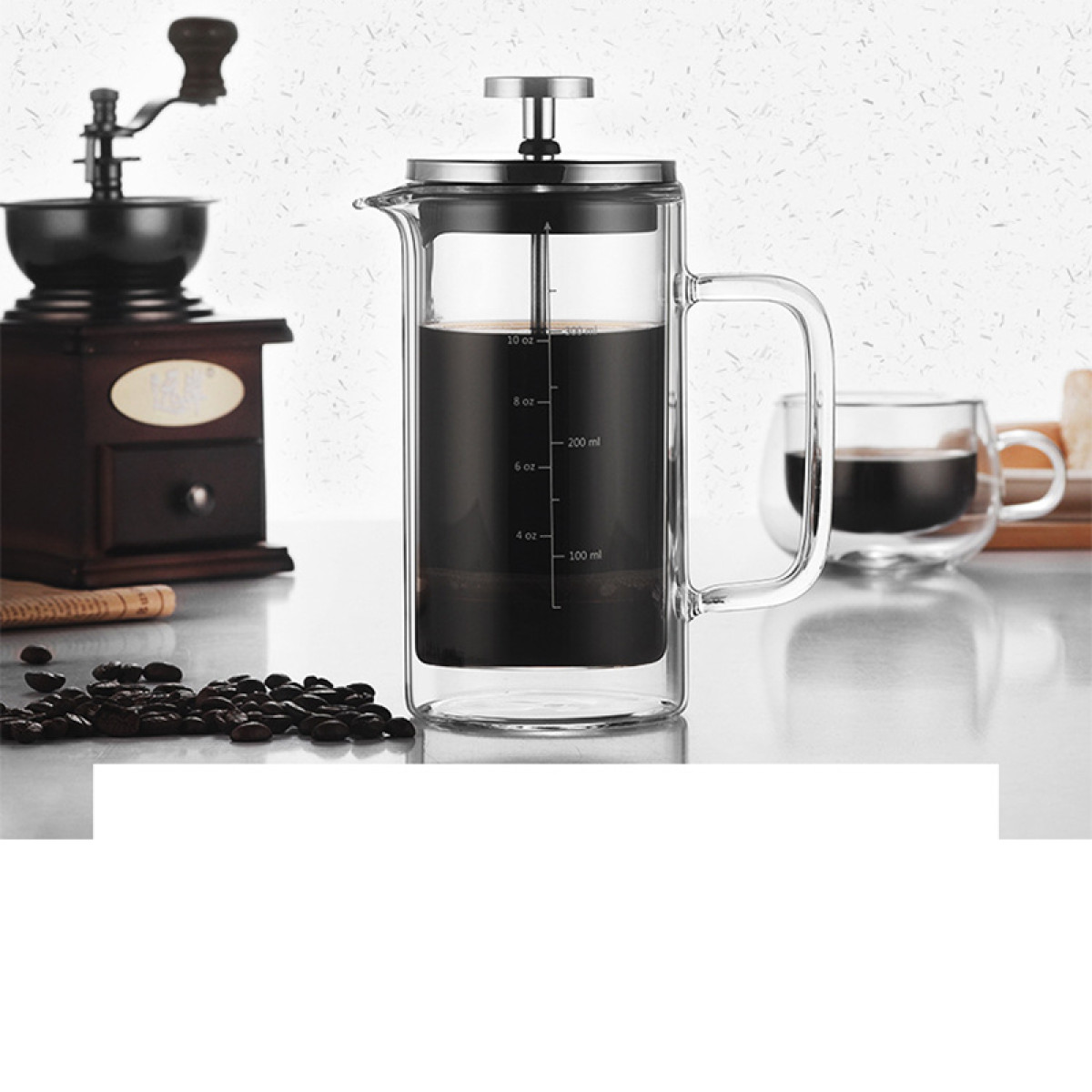Kaffeemühle, French Press mit Kaffee und eine Tasse daneben, mit Bohnen im Vordergrund.
