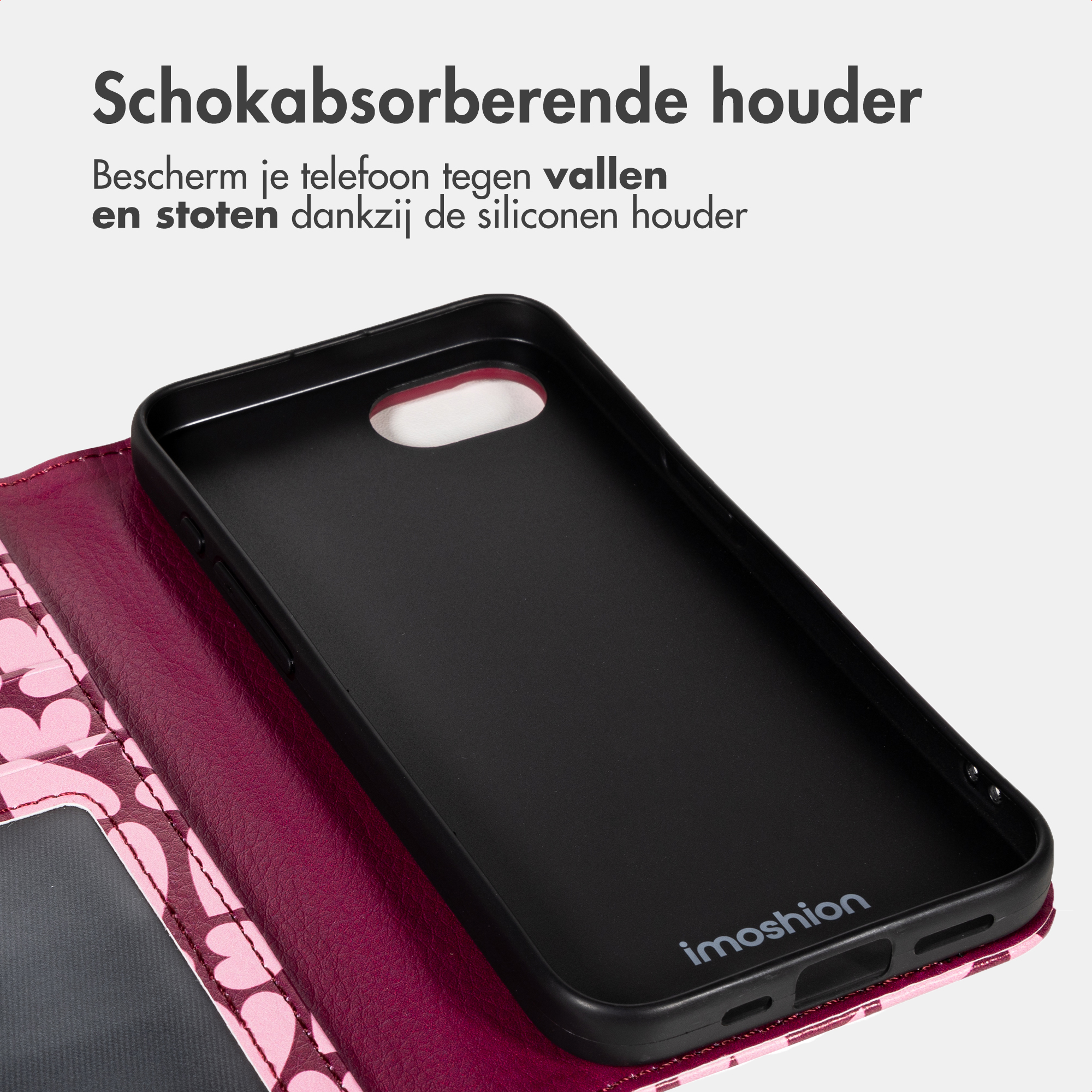 A black phone case lies on a pink heart-patterned wallet case, with Dutch text about shock absorption above.
