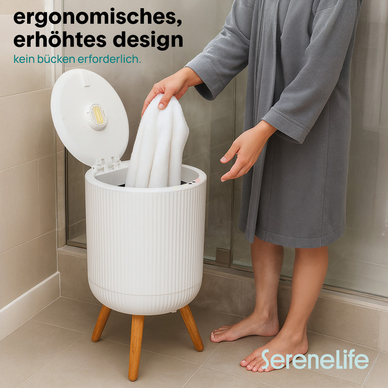 Eine Person im Bademantel legt ein weißes Handtuch in einen weißen Wäschebehälter auf Holzbeinen.