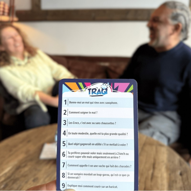 Person hält Spielkarte mit Fragen. Zwei Personen im Hintergrund.
