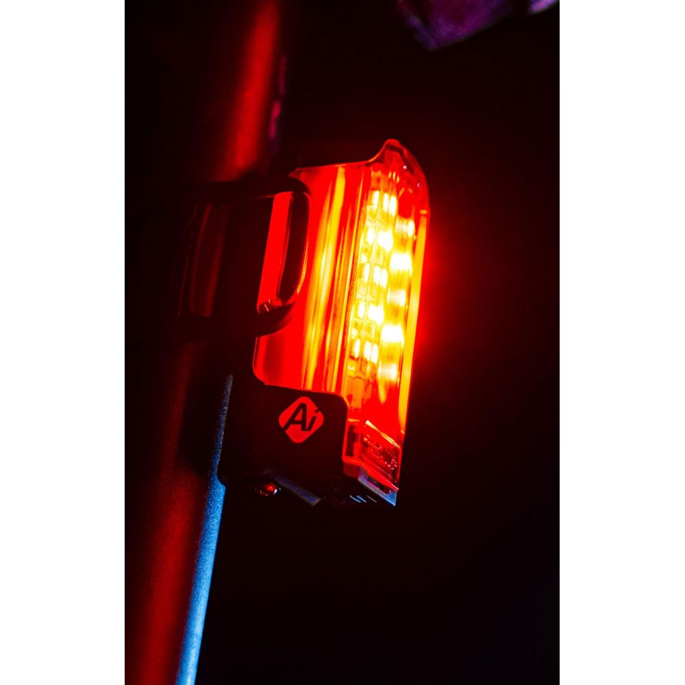 Ein rotes LED-Fahrradrücklicht mit schwarzer Halterung an einer dunklen Stange.