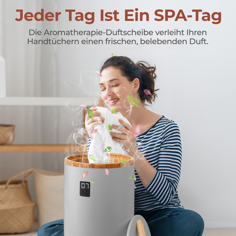 Eine Frau lächelt mit geschlossenen Augen und hält ein weißes Tuch über einem grauen Dampfgarer mit Holzrand. Blätter und Blütenblätter schweben um sie herum.