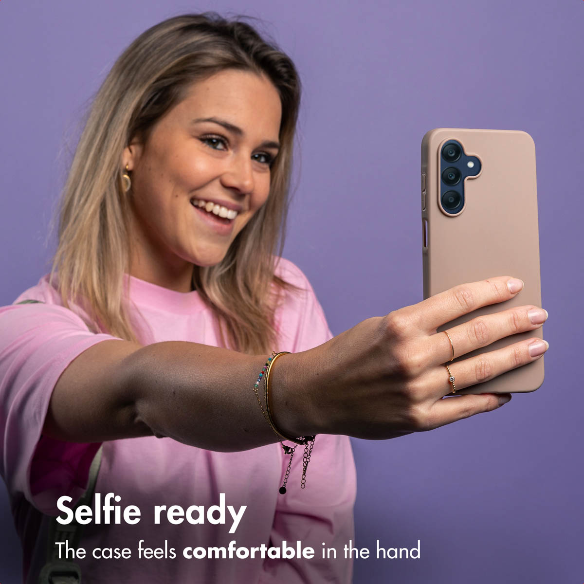 Woman takes a selfie with a pink phone against a purple background.