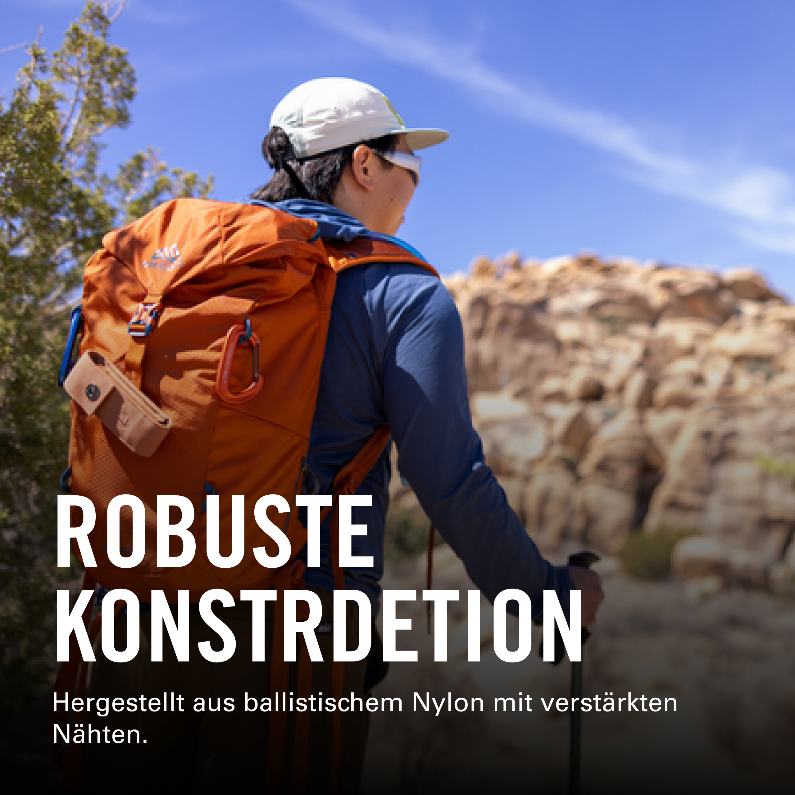 Eine Person mit orangefarbenem Rucksack und weißer Mütze wandert an einem sonnigen Tag mit felsigem Gelände im Hintergrund.
