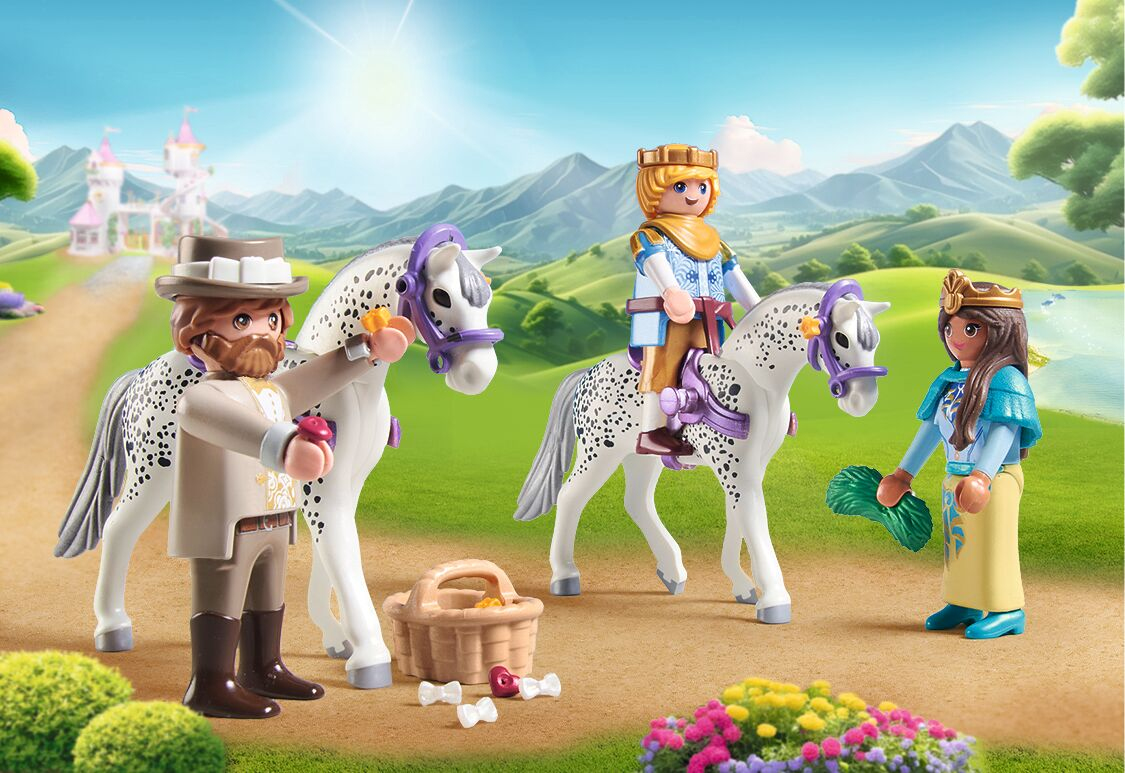 Drie Playmobil-figuren en twee gevlekte paarden op een zandpad met een kasteel en bergen op de achtergrond.