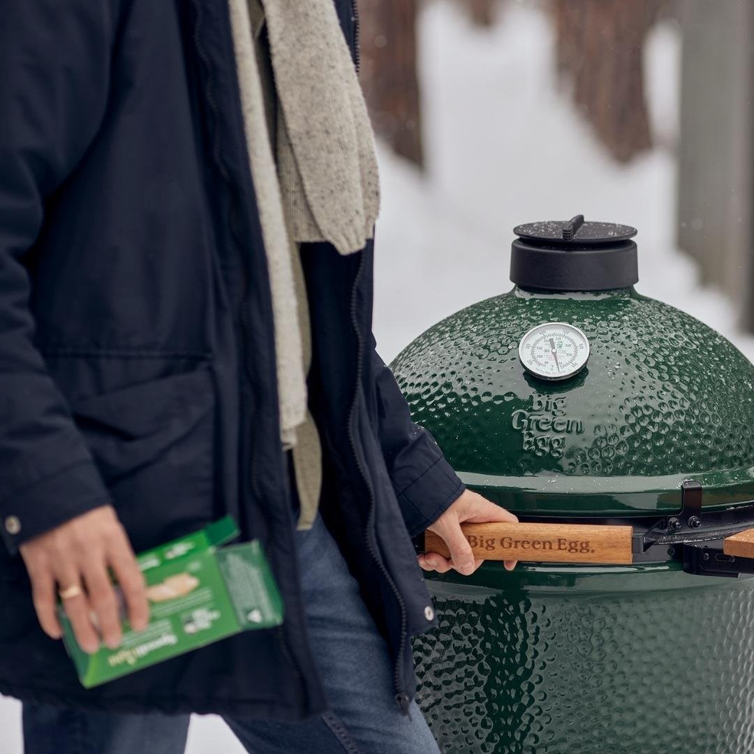 Ceketli ve şallı kişi karda Big Green Egg ızgarayı açıyor.