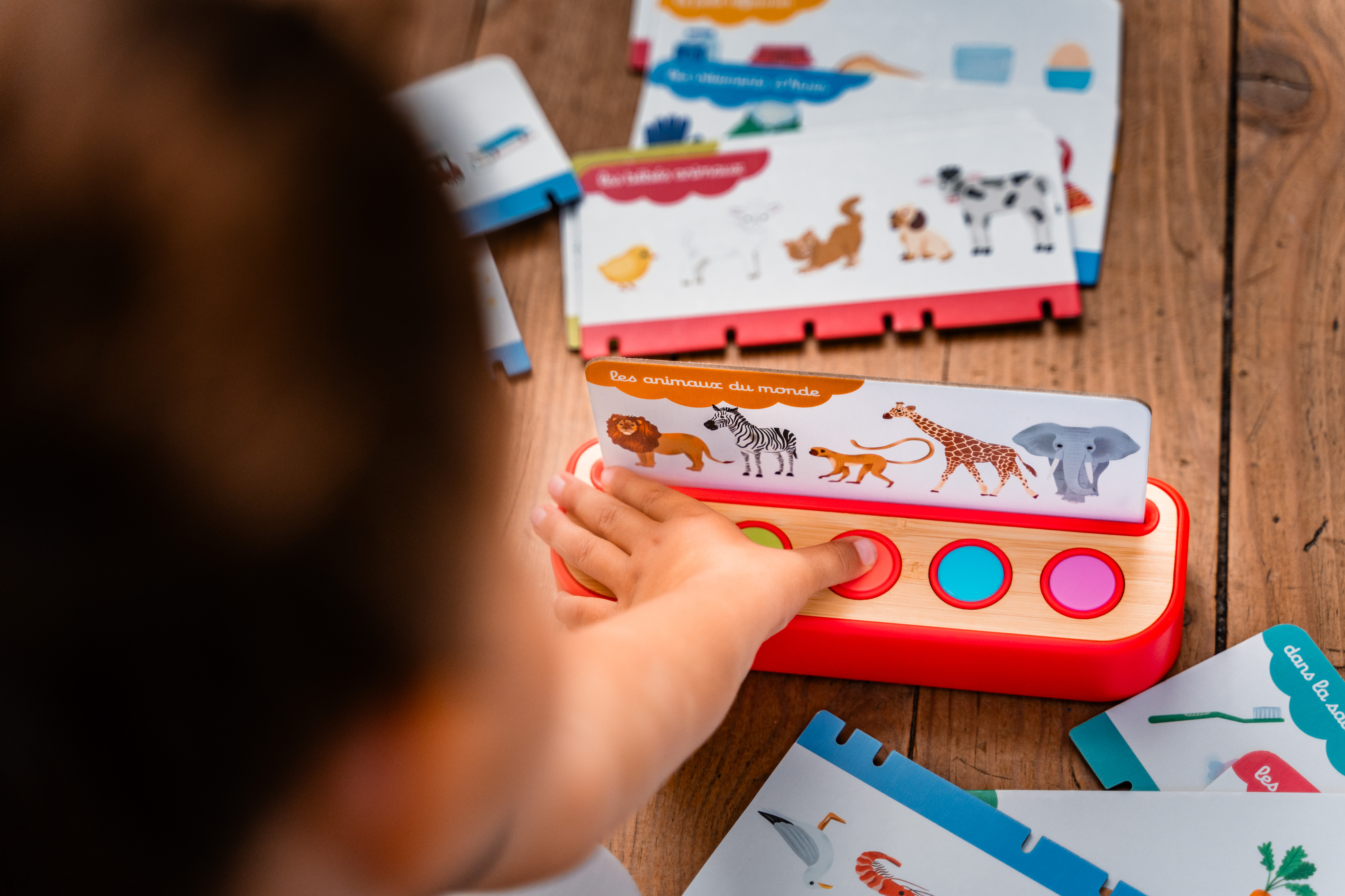 Ein Kind drückt auf einen roten Knopf eines Spielzeugs mit Tiermotiven.