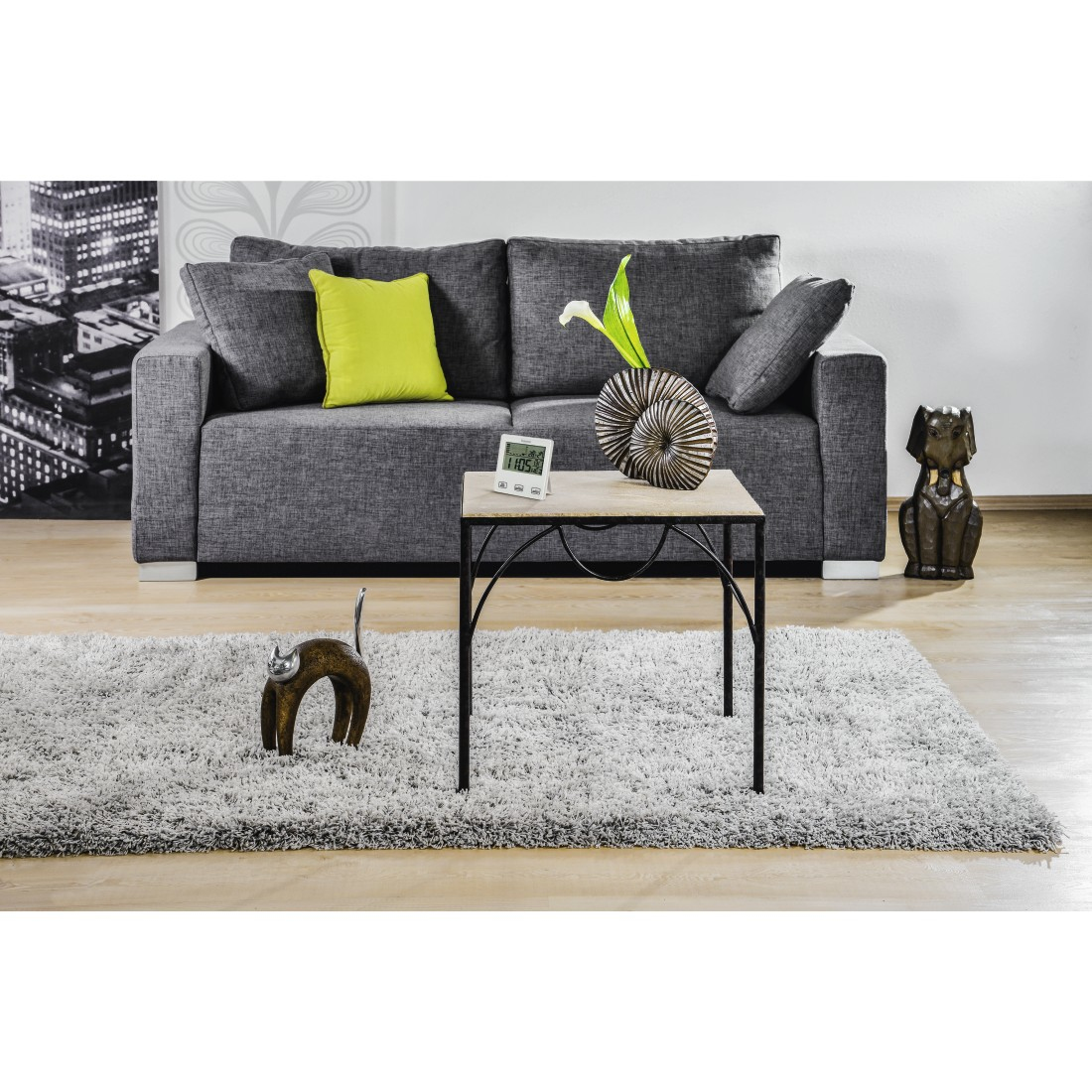 Graues Sofa mit einem hellgrünen Kissen, Couchtisch mit Deko und Uhr, Teppich und Deko-Hund.
