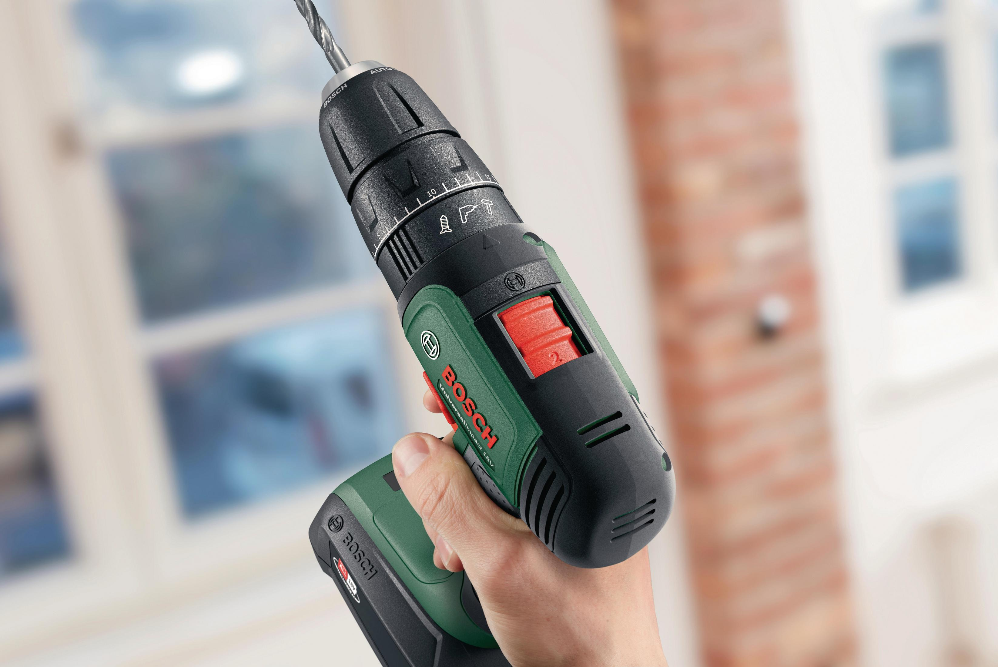 Eine Hand hält eine grün-schwarze Bosch UniversalImpact 18V Bohrmaschine mit Metallbohrer vor verschwommenem Hintergrund.