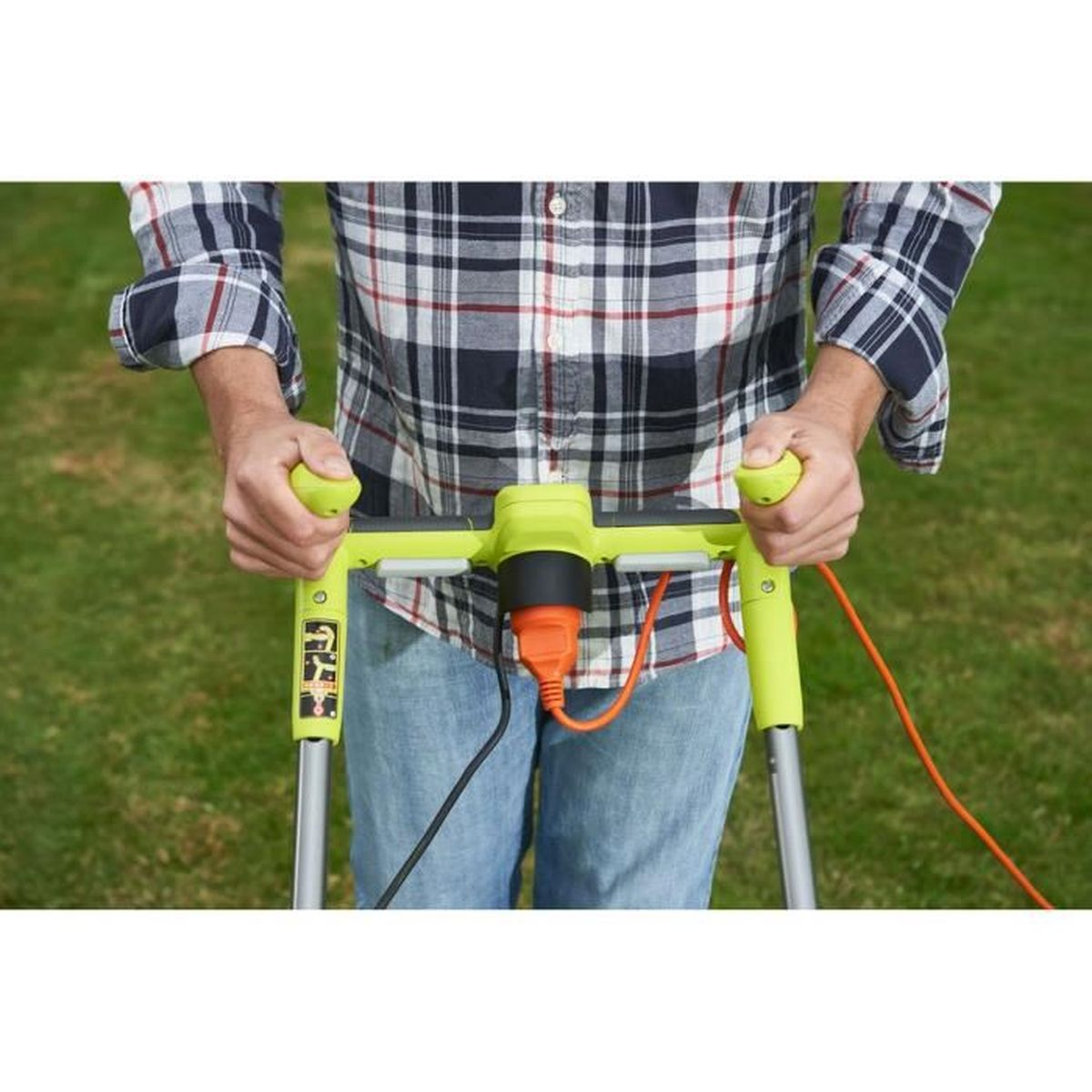 Eine Person in einem karierten Hemd und Jeans hält die leuchtend grünen Griffe eines elektrischen Rasentrimmers mit einem orangefarbenen Kabel.