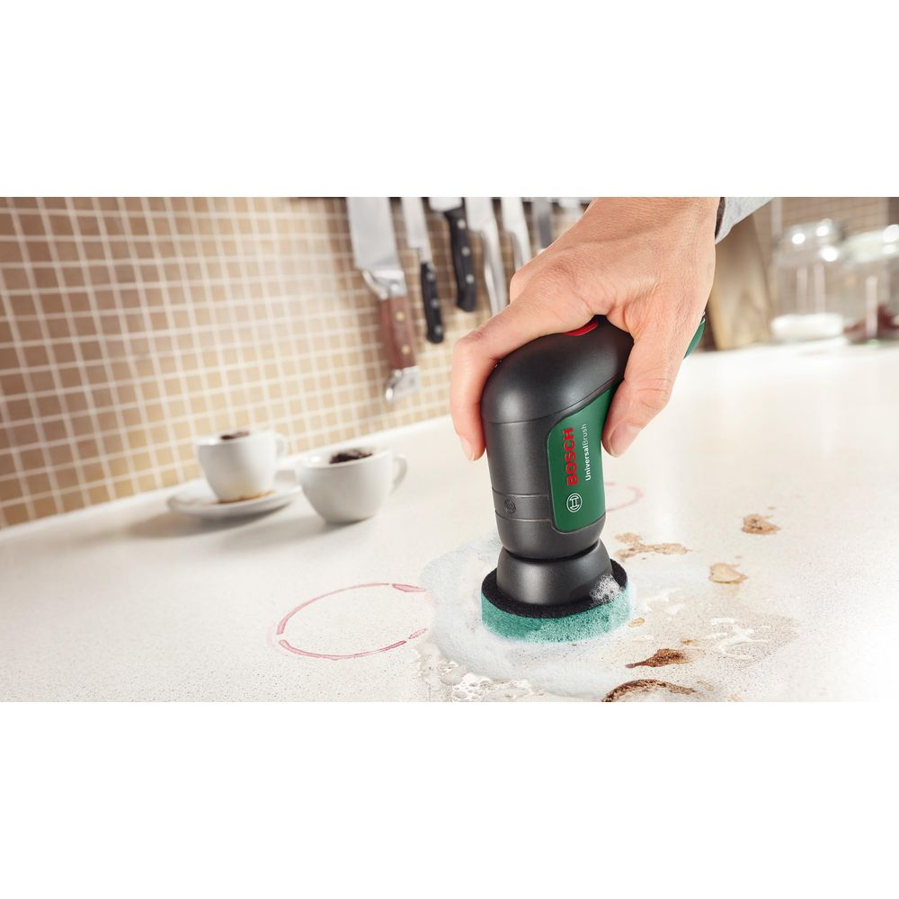 Hand mit Bosch-Reiniger reinigt Flecken auf einer Arbeitsplatte. Zwei Tassen im Hintergrund.
