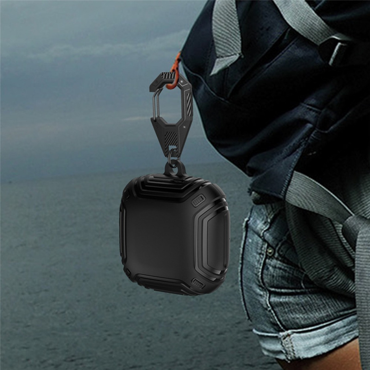 Ein schwarzes Schutzetui, möglicherweise für Kopfhörer, hängt an einem dunkelgrauen Karabiner, der an einem Rucksackriemen befestigt ist.