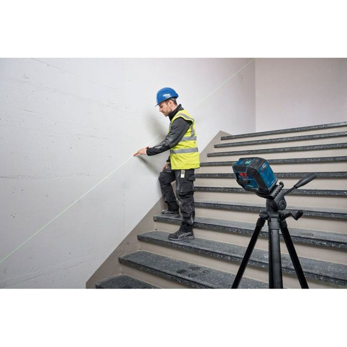 Mann auf Treppe mit Laser-Wasserwaage auf Stativ, der eine Linie an der Wand markiert.
