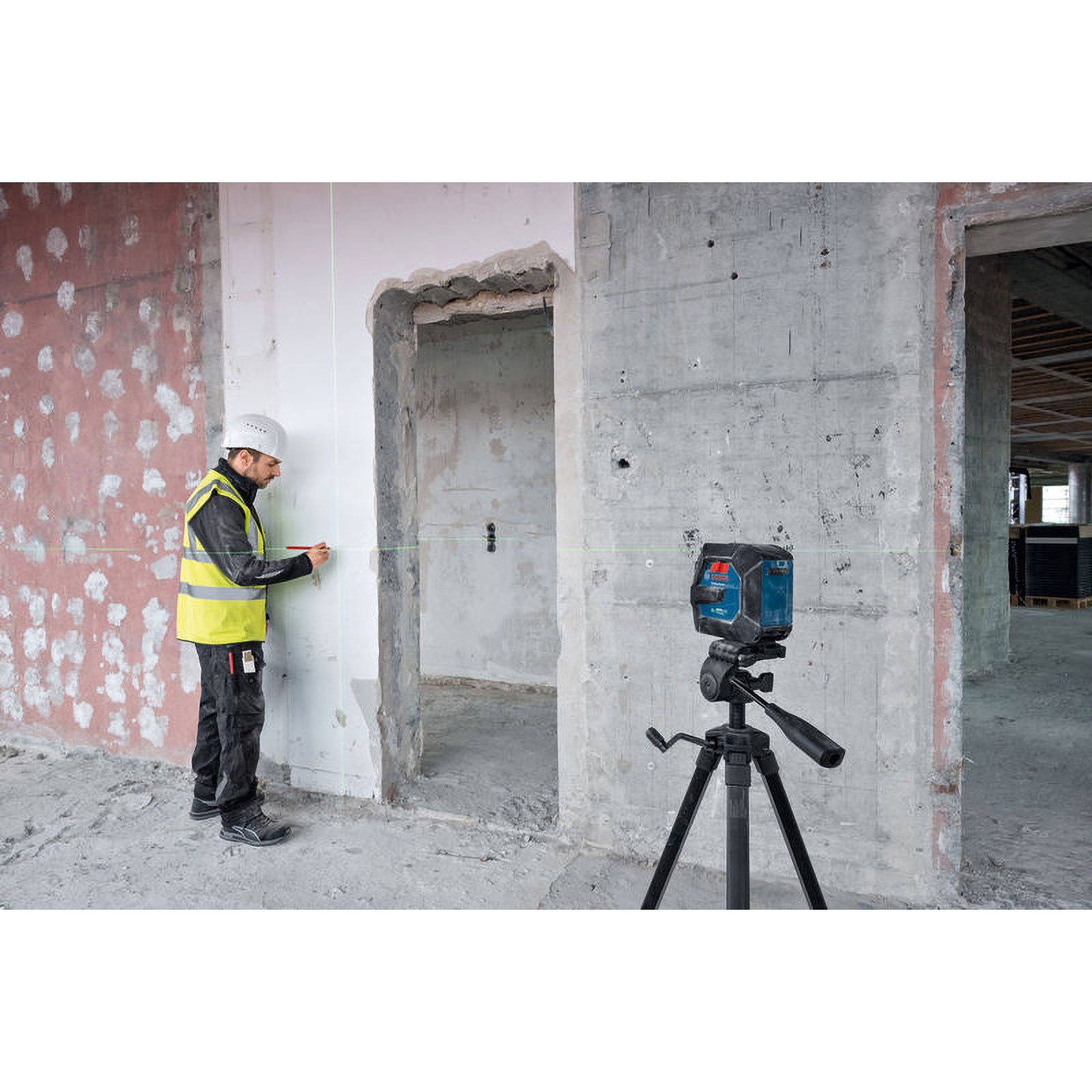 Bauarbeiter in Warnweste benutzt Laser-Nivelliergerät auf Baustelle. Stativ mit Gerät sichtbar.