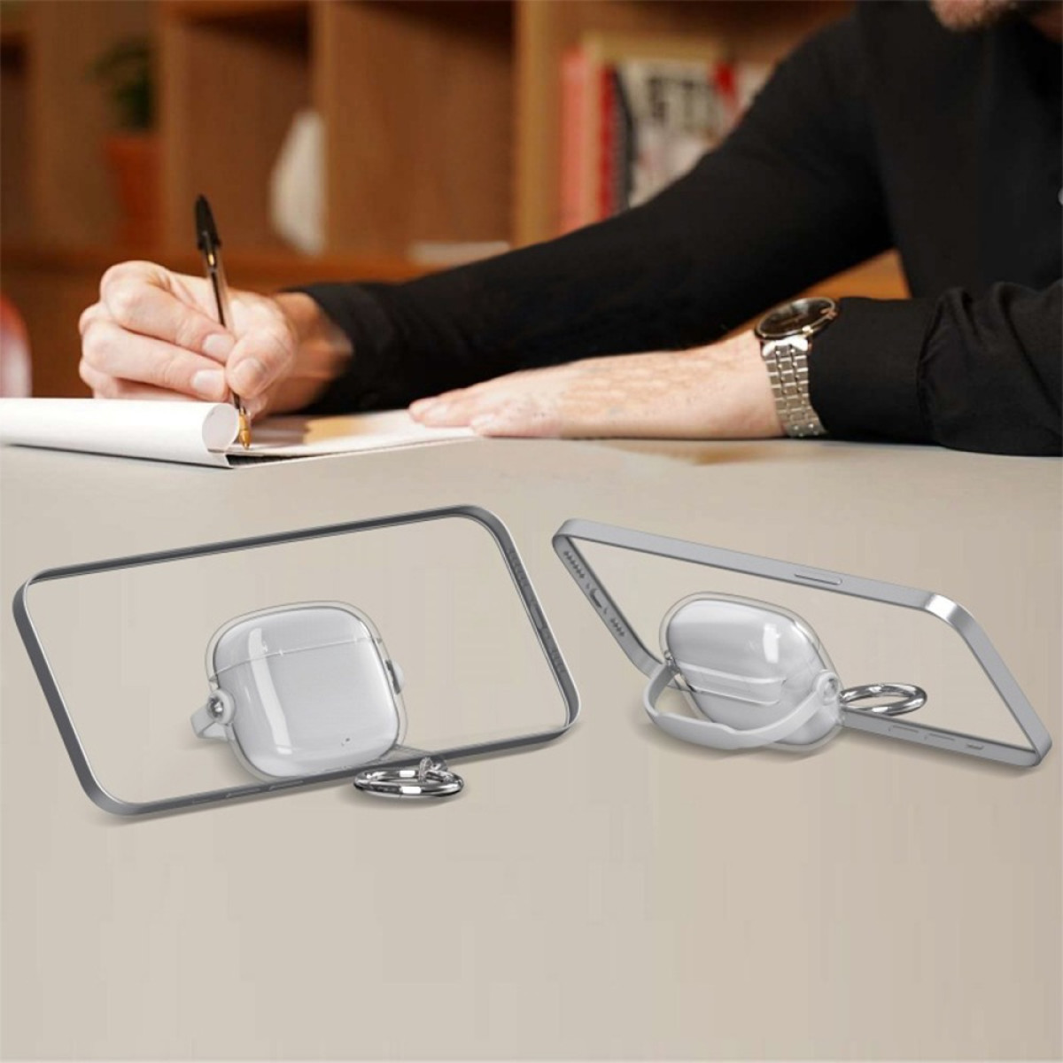 Una persona scrive su un quaderno, mentre due custodie trasparenti per AirPods sono esposte su una superficie chiara.