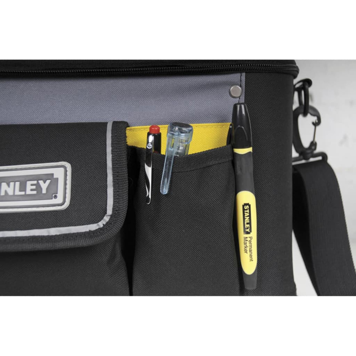 Nahaufnahme einer schwarz-grauen Stanley-Werkzeugtasche mit einem gelben Permanentmarker, einem Stift und einem durchsichtigen Werkzeug in den Taschen.