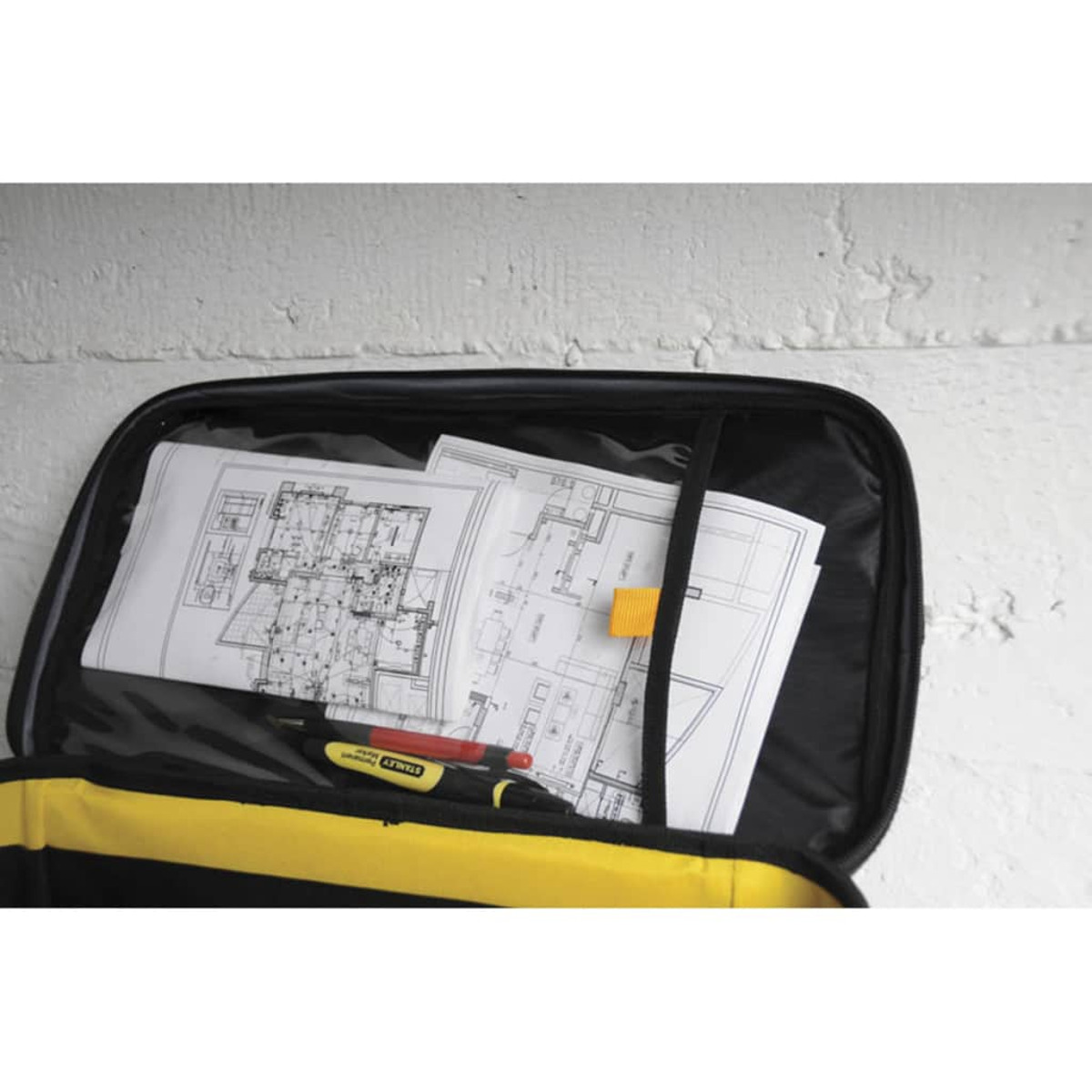 Eine offene schwarz-gelbe Werkzeugtasche zeigt architektonische Baupläne und einen rot-schwarzen Marker im Inneren.