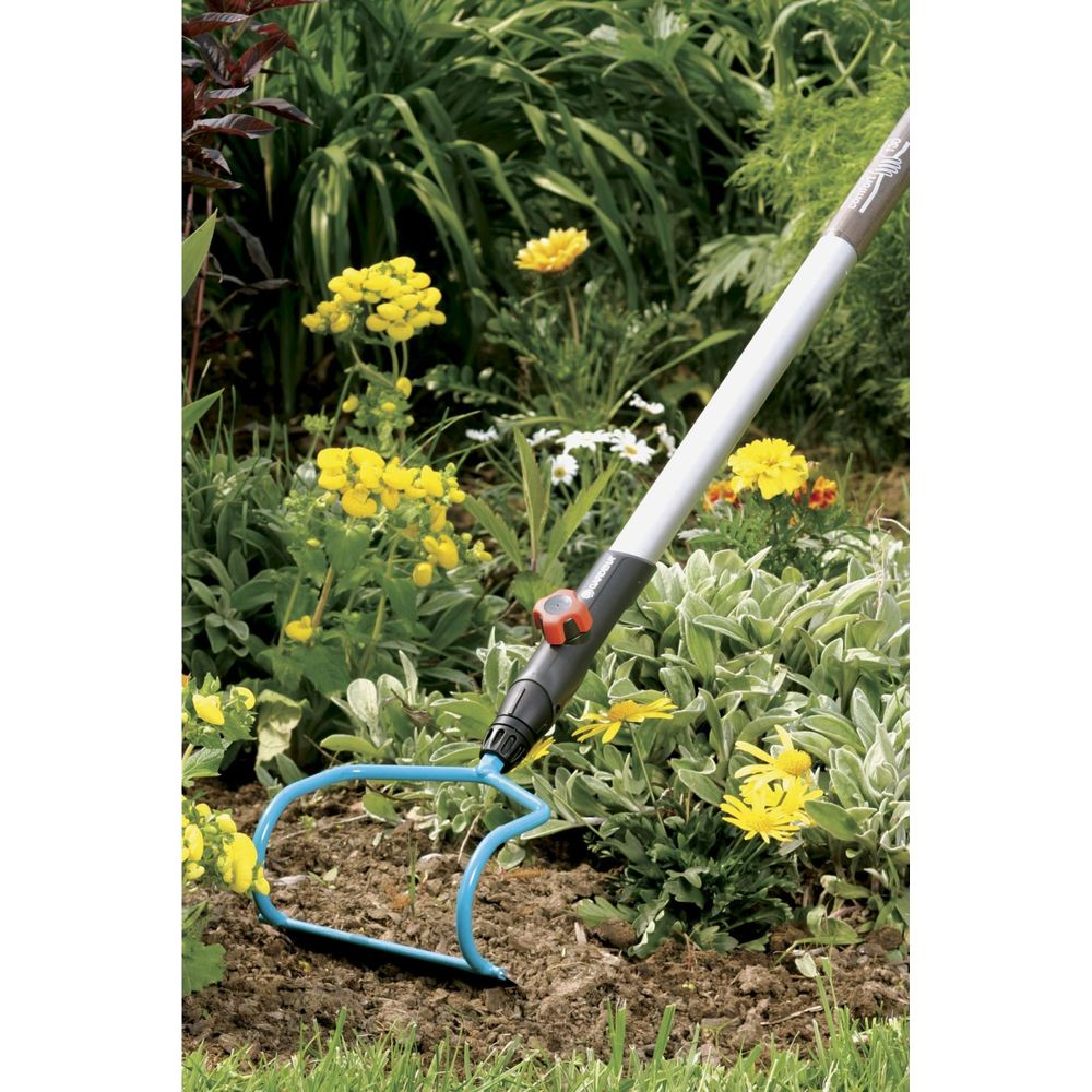Gartengerät mit blauem Metallkopf und grauem Stiel in einem Blumenbeet.