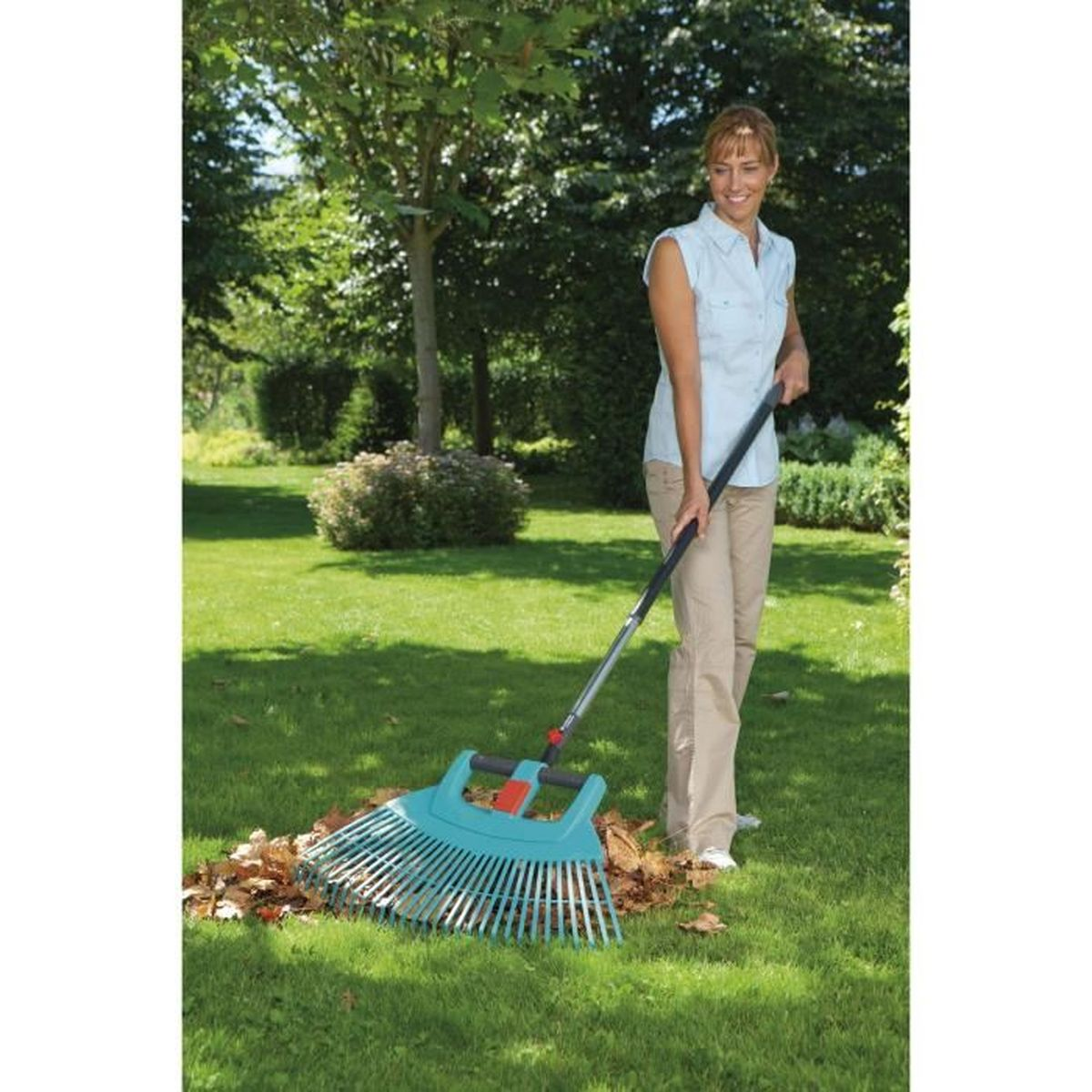 Eine Frau harkt im Garten Laub mit einem blauen Laubrechen.