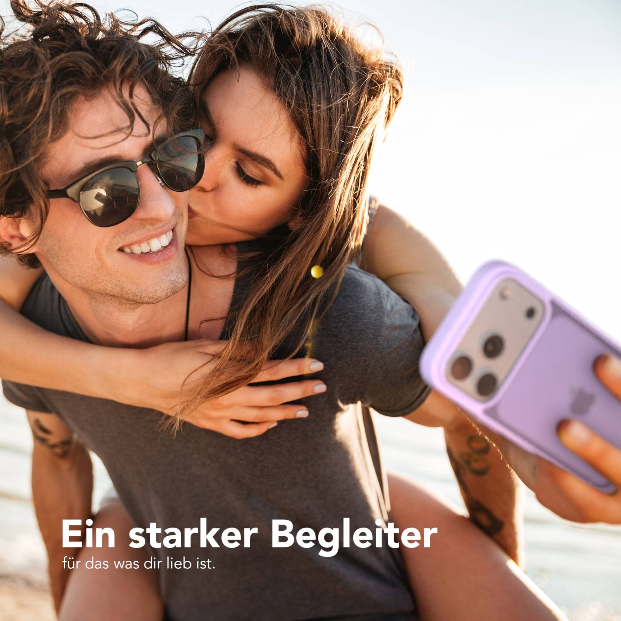 Ein Mann mit Sonnenbrille, der eine Frau auf dem Arm trägt. Sie küsst ihn.