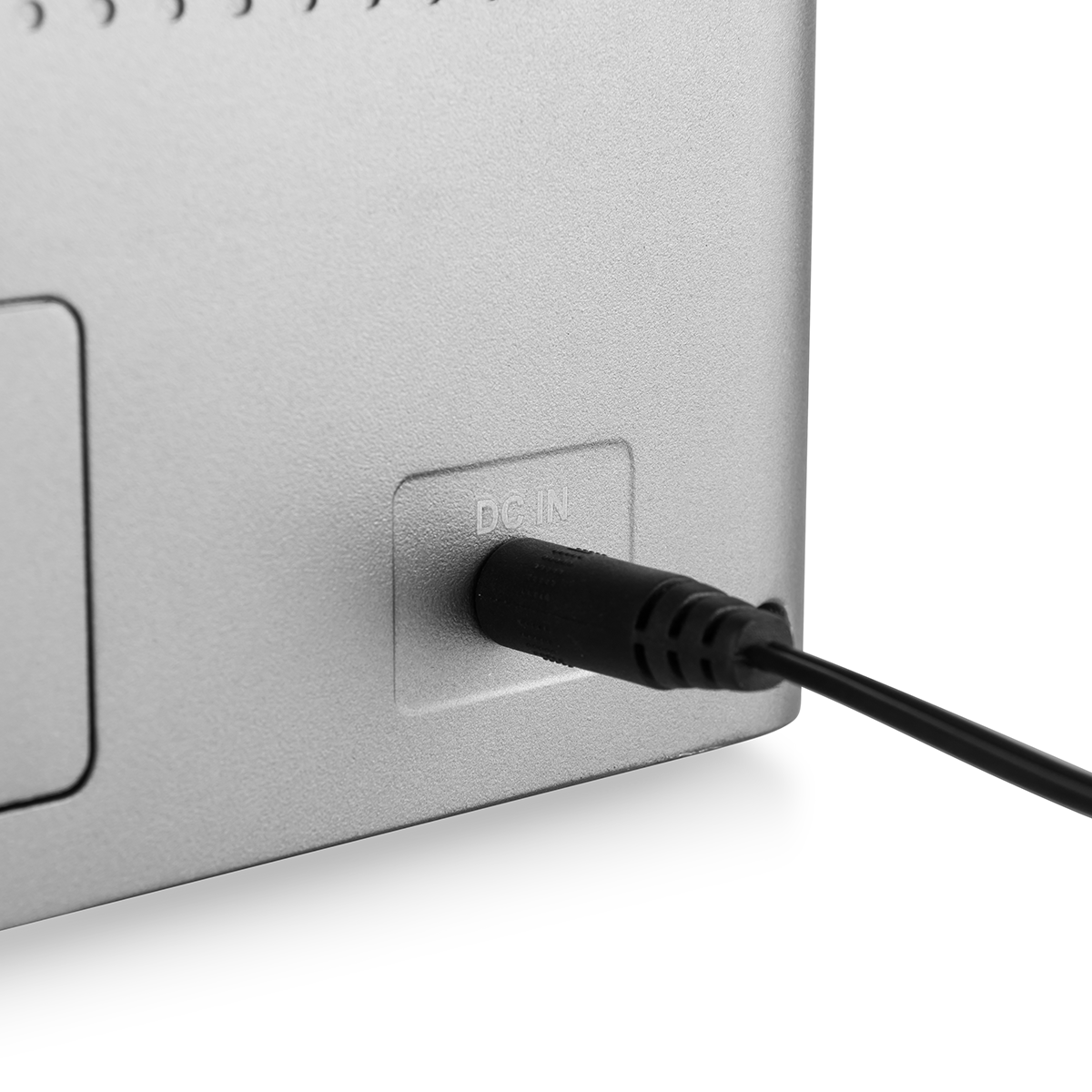 Zbliżenie srebrnego urządzenia elektronicznego z czarnym kablem zasilającym DC IN podłączonym do portu na białym tle.