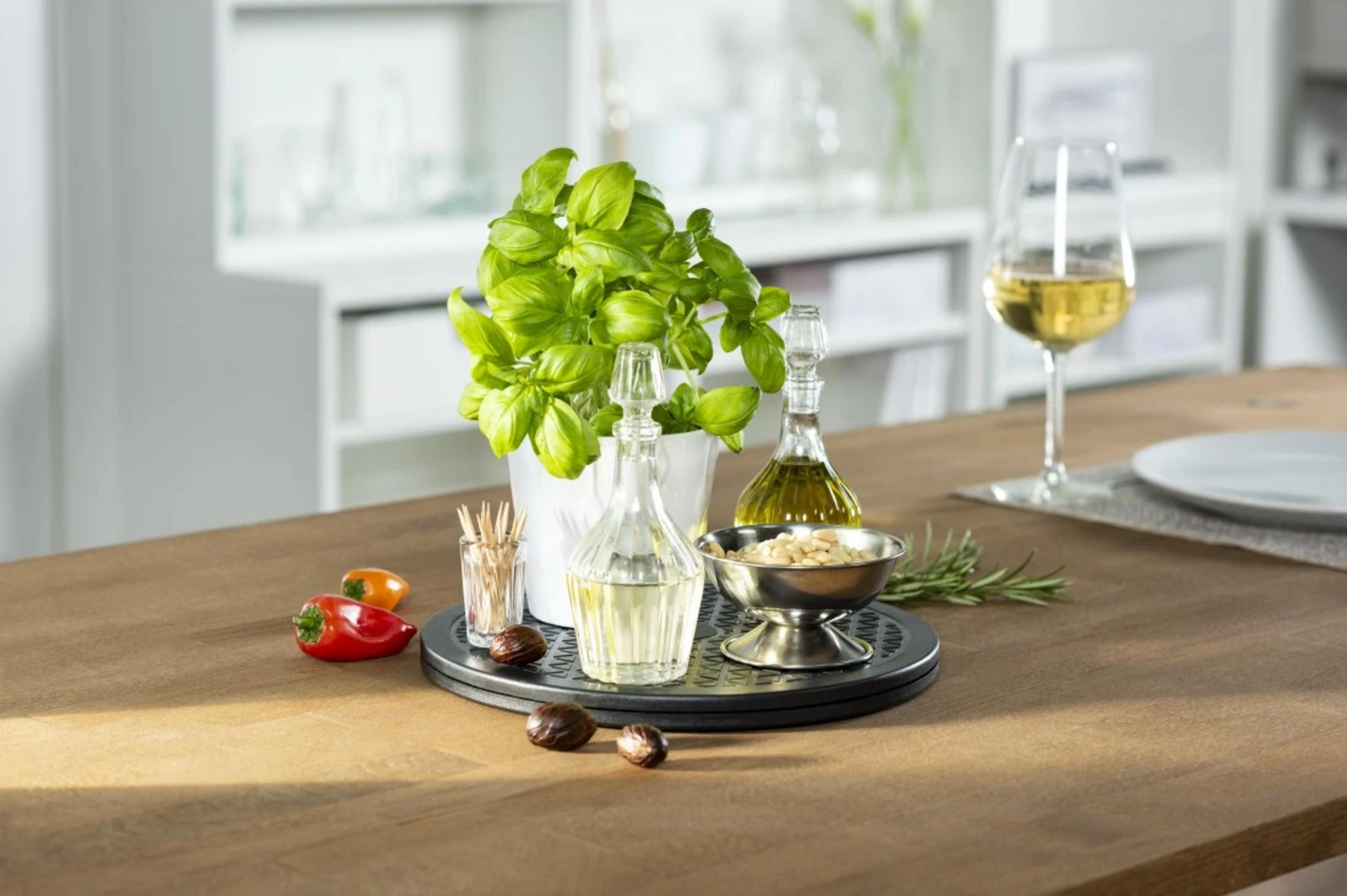 Basilico in vaso, bottiglie d'olio, pinoli, spezie, peperoni, vino e piatto.